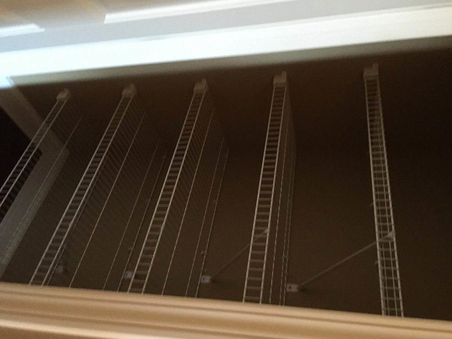Metal ladder leaning against built-in shelving in a closet with brown tile flooring and white walls, steel window frame visible in background.