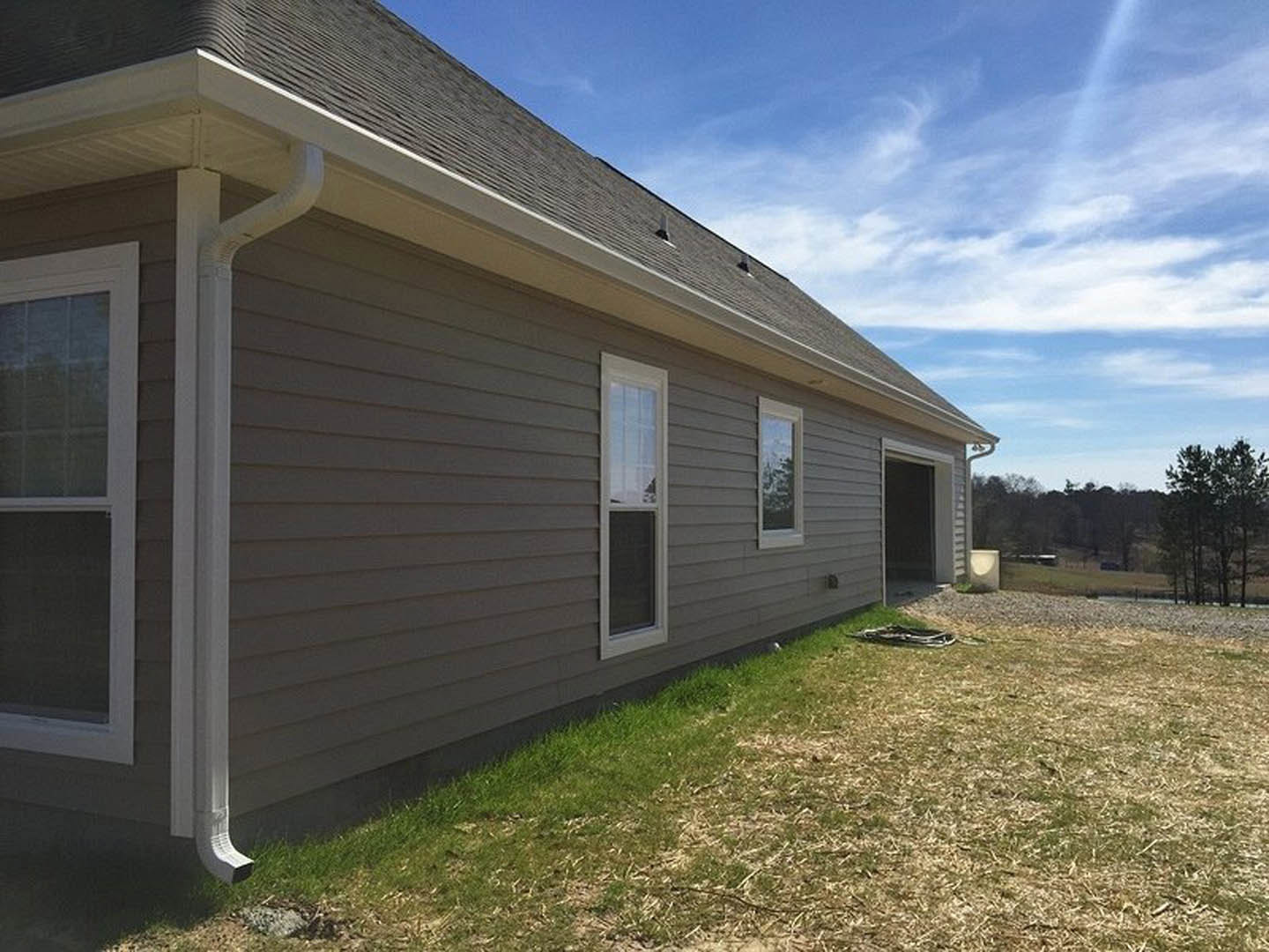 Two-story home with gray siding, attached garage, white-trimmed windows, covered front porch, manicured lawn, and mature tree in foreground