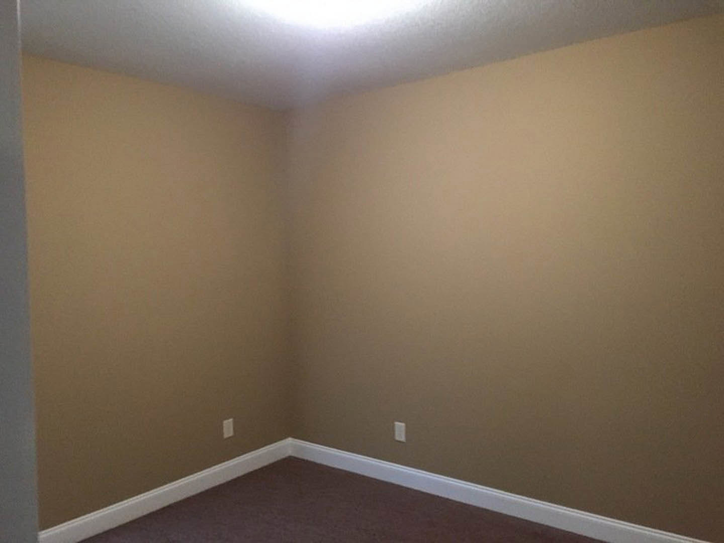 Corner of a room with light gray plaster walls, white ceiling, wall-mounted sconce, and soft beige carpet flooring