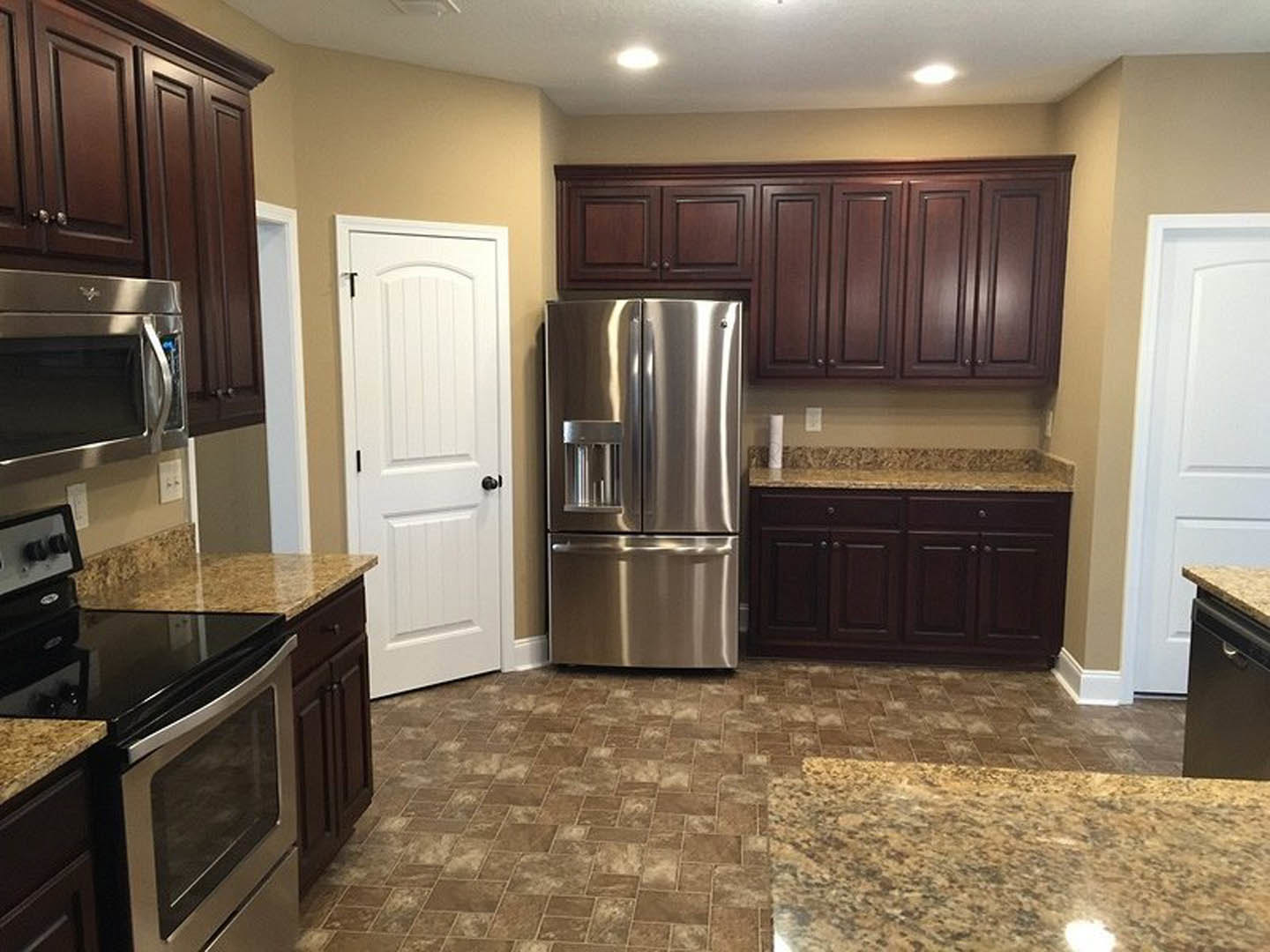 Kitchen with stainless steel refrigerator, built-in microwave, granite countertops, wood cabinetry, and white door with black knobs