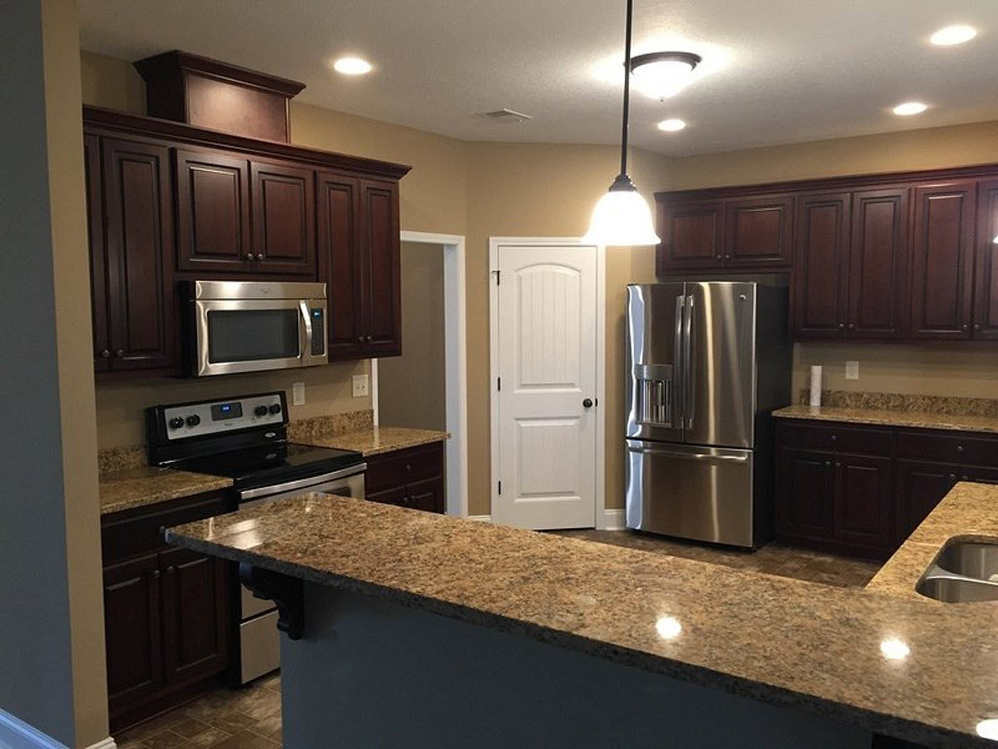 Granite countertops, stainless steel refrigerator and microwave, white cabinetry, black hardware, bright overhead lighting in modern kitchen