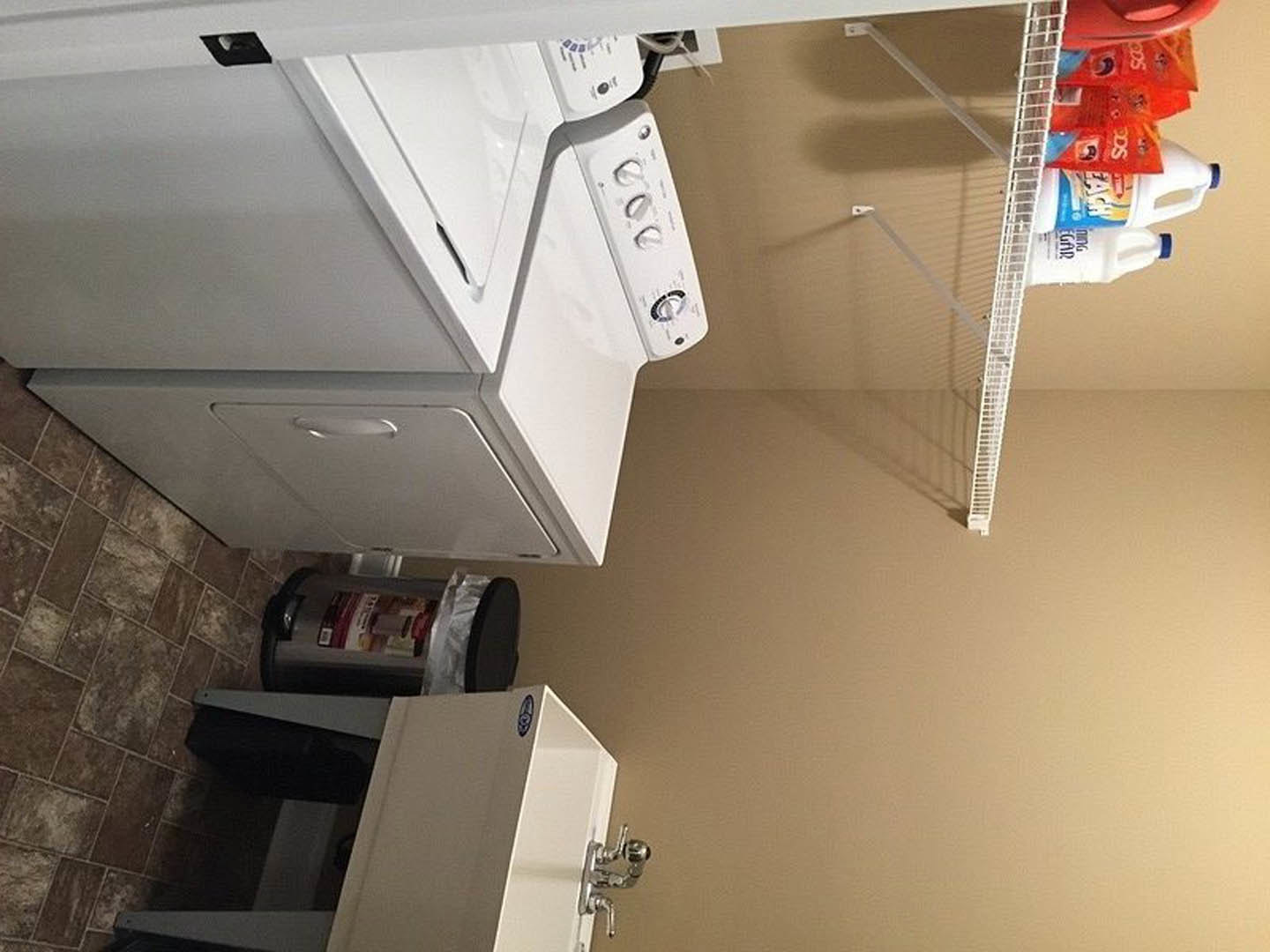 Laundry room with white front-loading washer and dryer set against light plaster walls, built-in cabinetry above appliances, and tile flooring