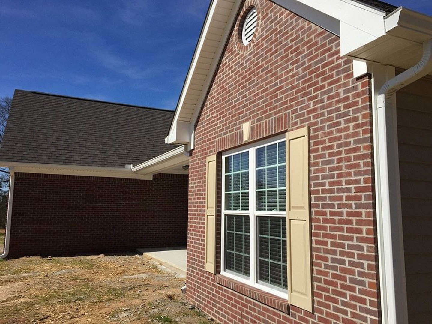 Red brick exterior with white roof, large window framed in white trim, dirt landscaping in foreground, clear sky above