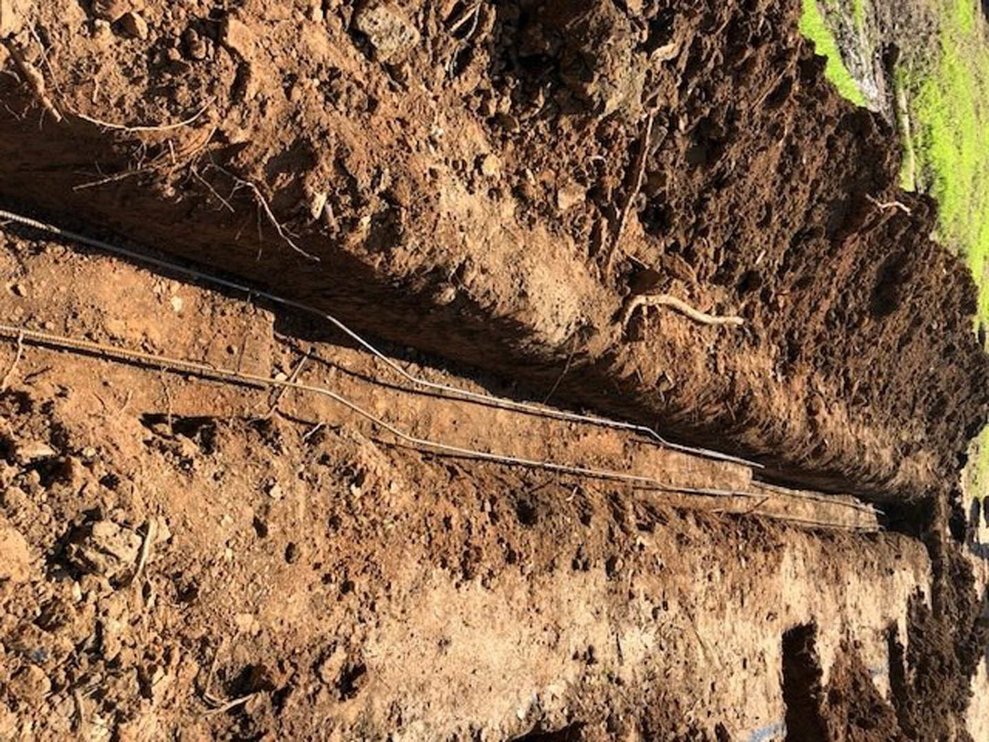 Exposed metal pipe embedded in compacted soil outdoors, surrounded by loose dirt and natural ground textures