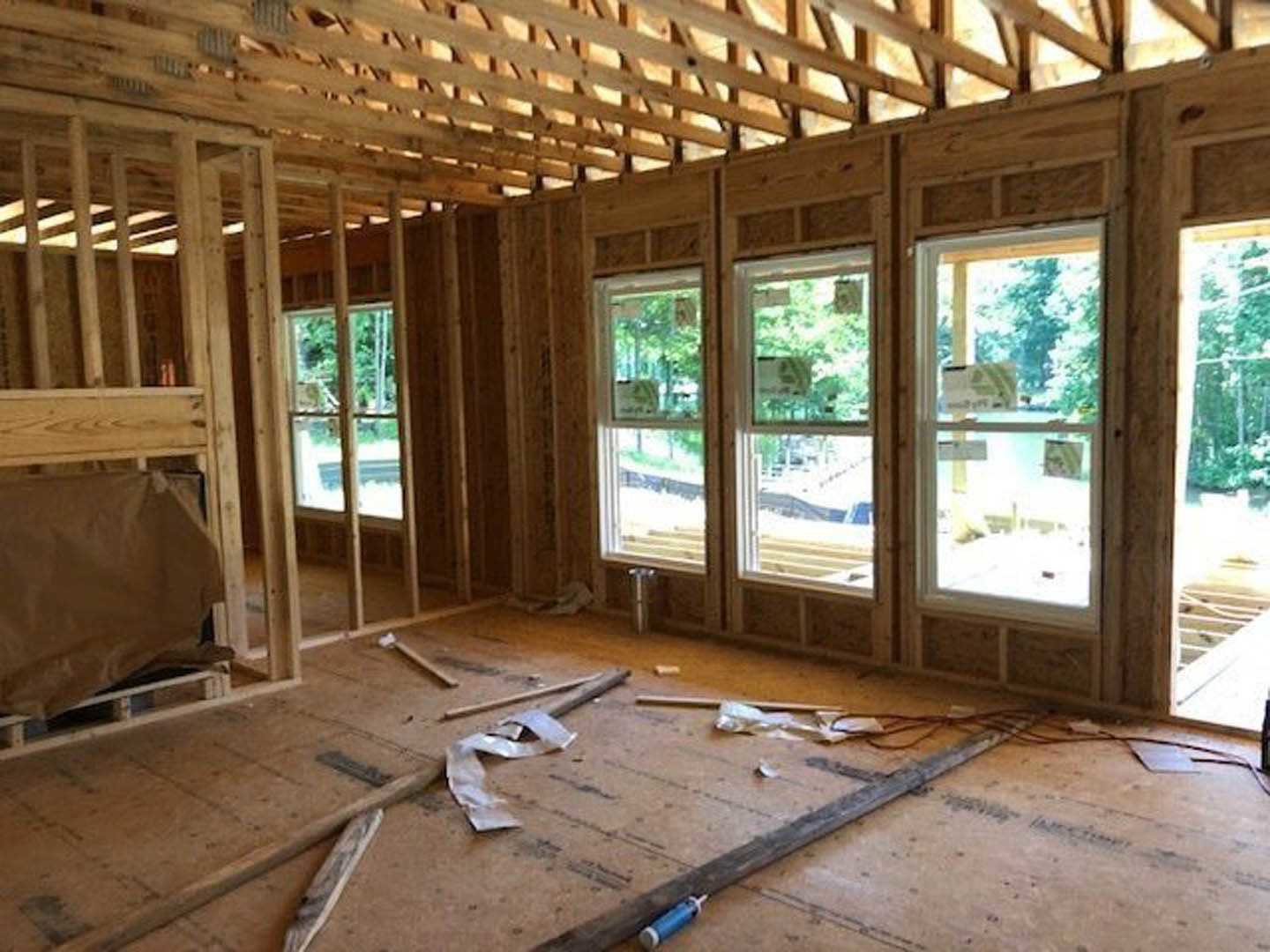 Open room with exposed wood ceiling beams, large windows, white metal frame supporting a brown paper bag, long wooden ruler and sheet of paper on light-colored floor, window with
