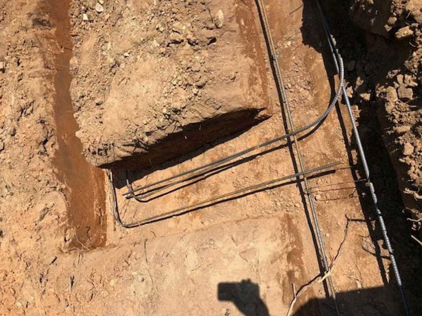Dirt ground with exposed metal pipes, scattered rocks, and visible soil textures