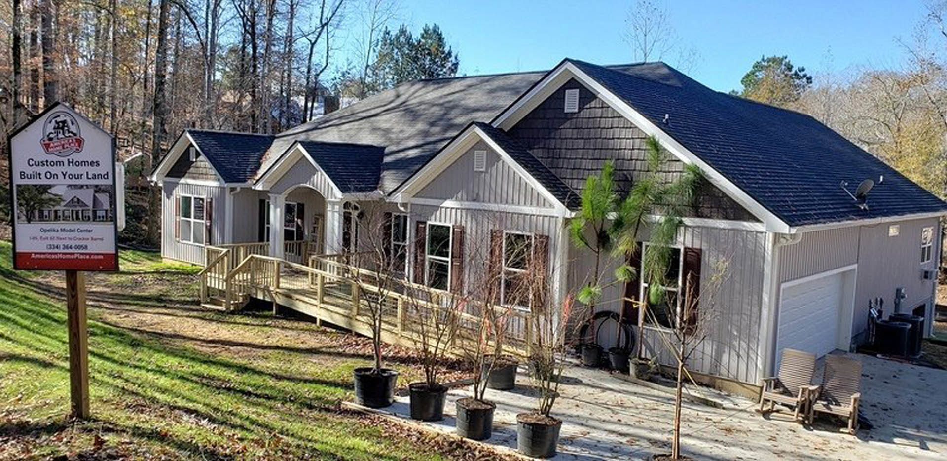 Modern cottage-style home with wood deck, large windows, and surrounding mature trees; patio features wooden chair and metal bucket, roof has dark shingles.