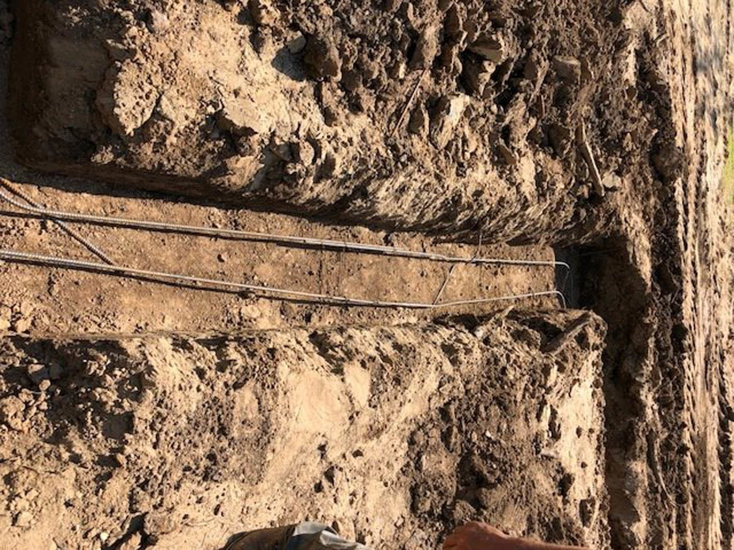 Trench dug in dirt with exposed metal rods, outdoor construction site
