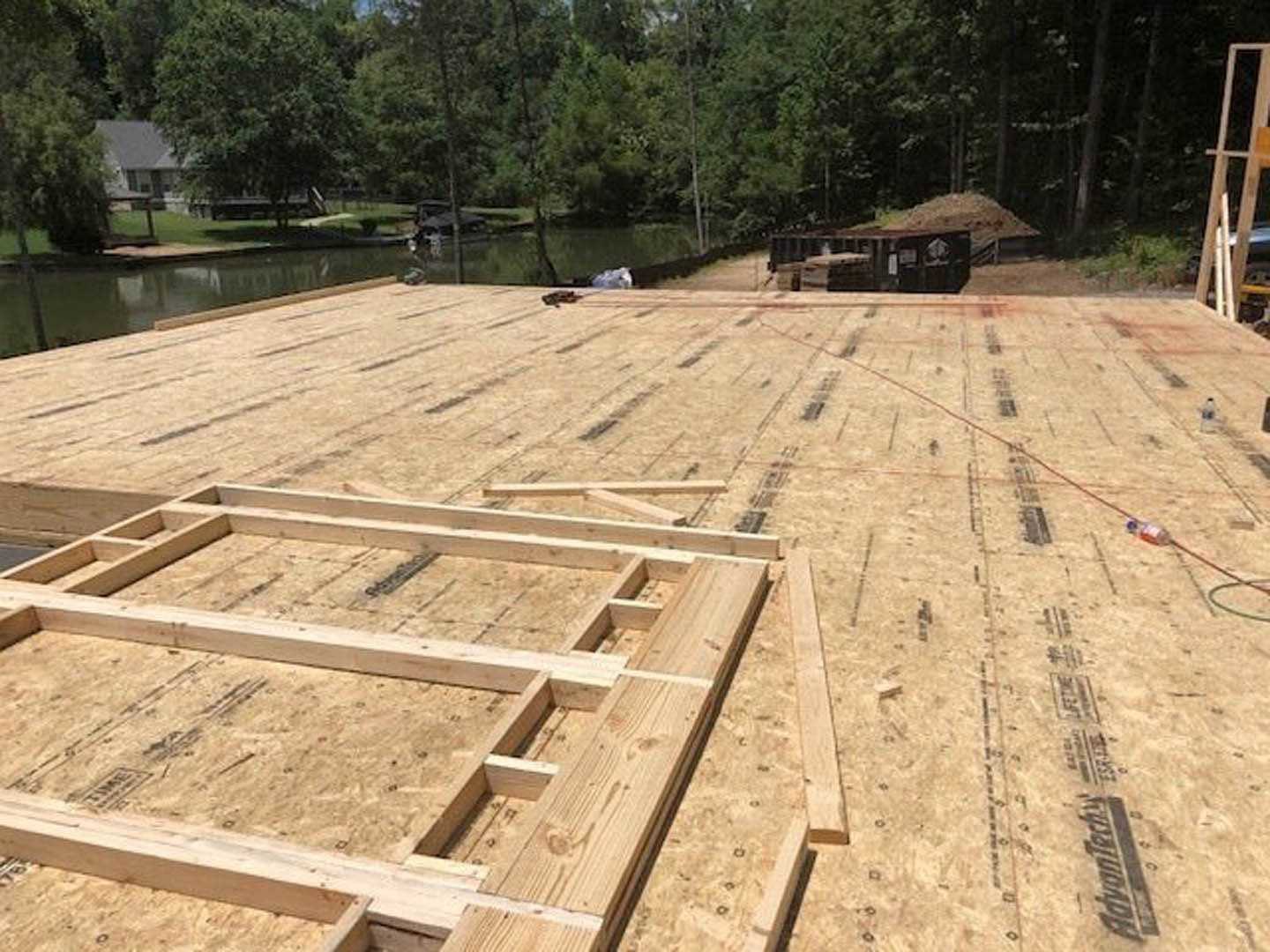 Exposed wooden framing of a house under construction, surrounded by trees and bare ground