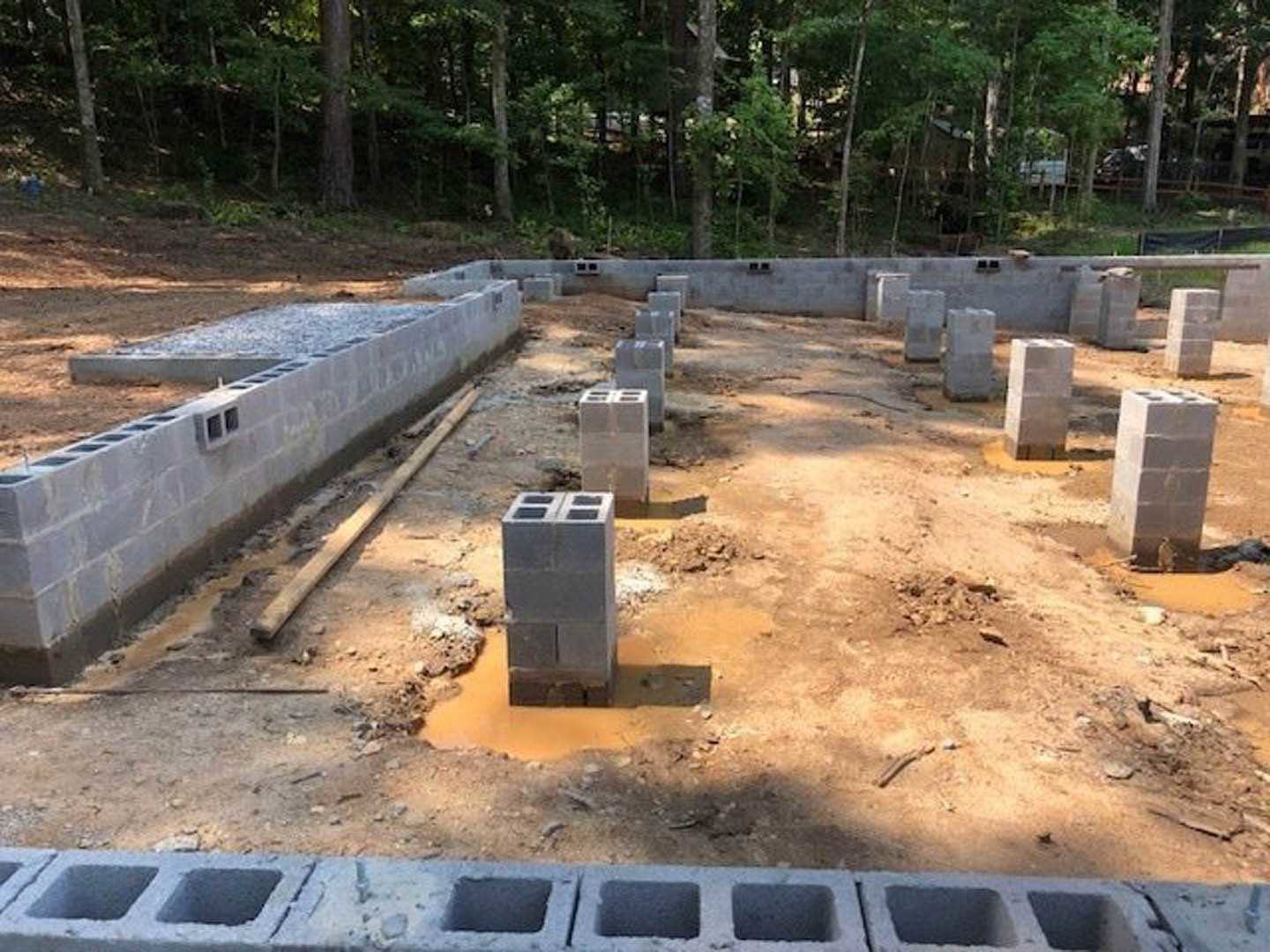 Concrete foundation with stacked concrete blocks set in the ground, surrounded by soil and trees in the background