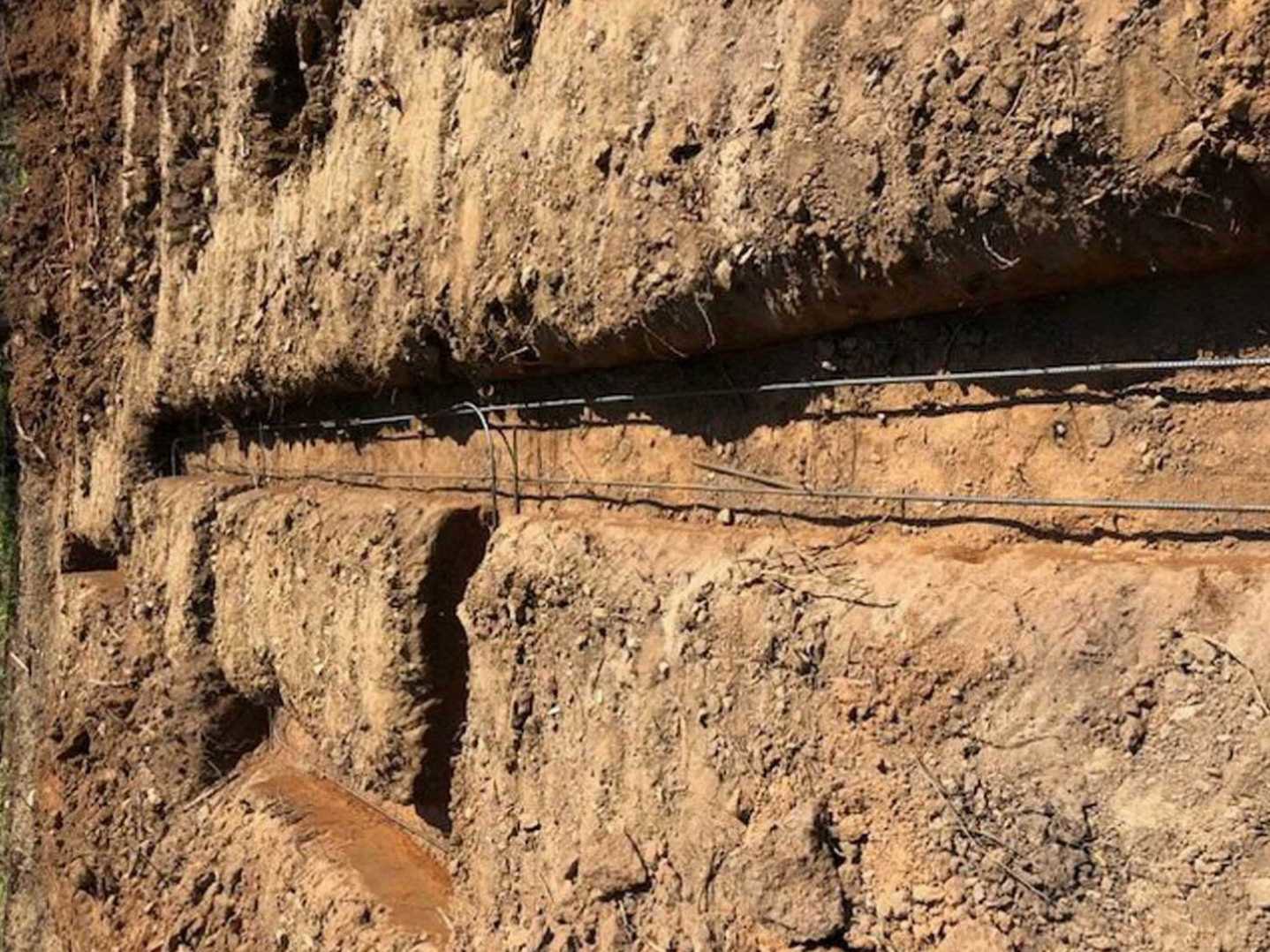 Brown dirt wall with exposed rocks and wire, trench detail, blurred shadow of person visible on surface