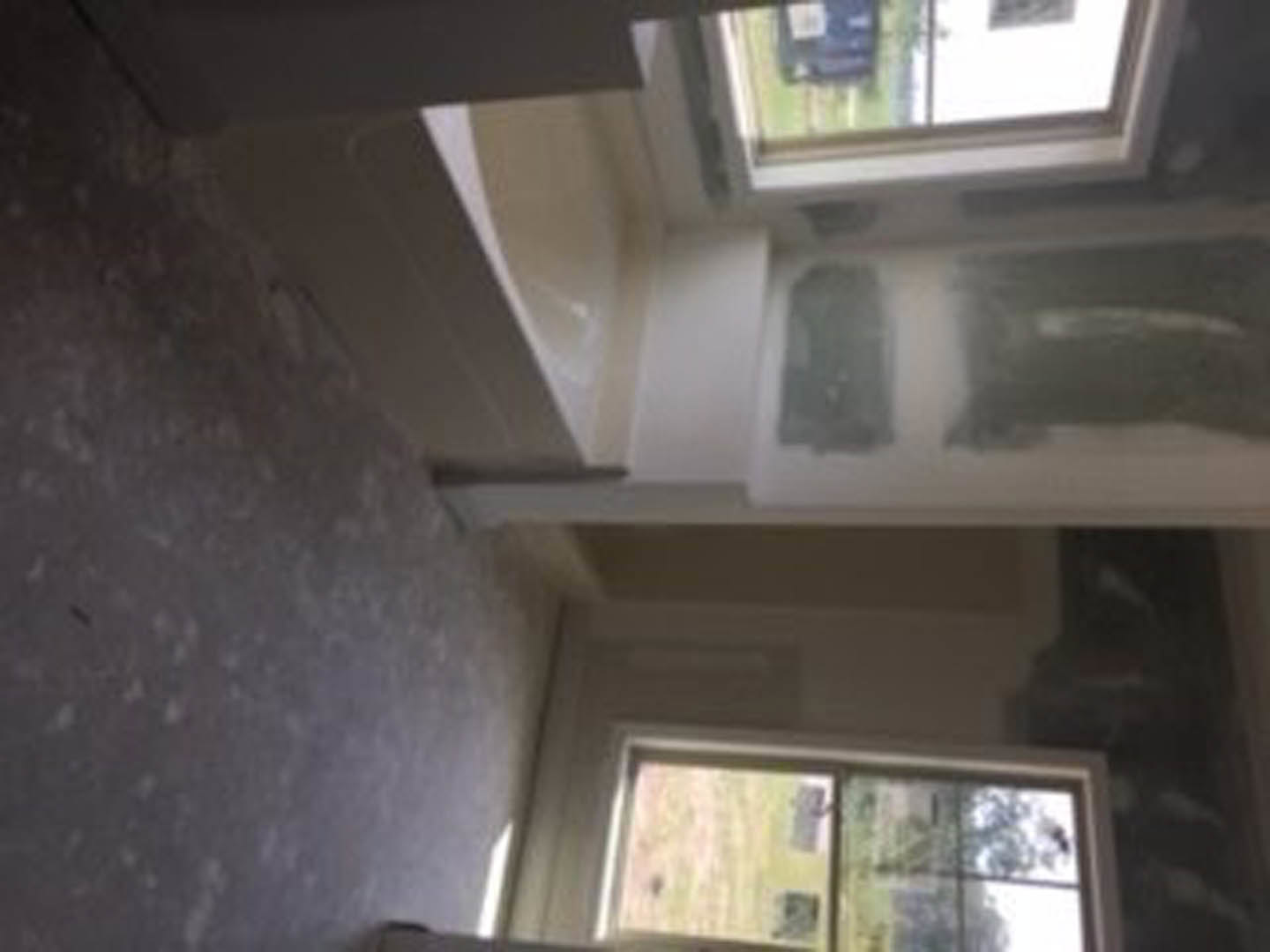 Freestanding white bathtub beneath large window, light gray tile flooring, white walls, chrome fixtures, natural daylight filling bathroom.