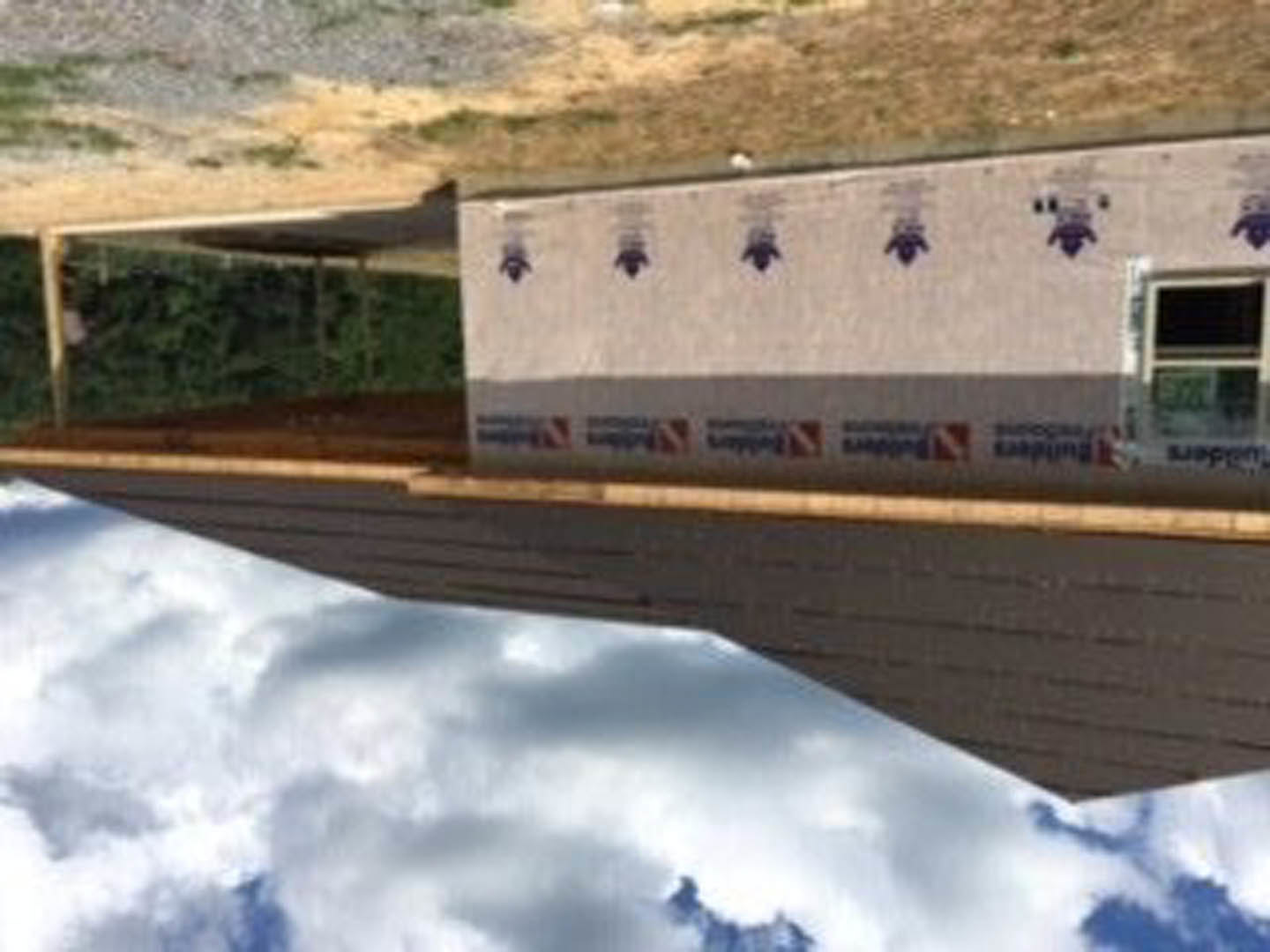 Two-story house with white siding, blue trim, and blue and white logo signs on exterior wall, under partly cloudy sky.