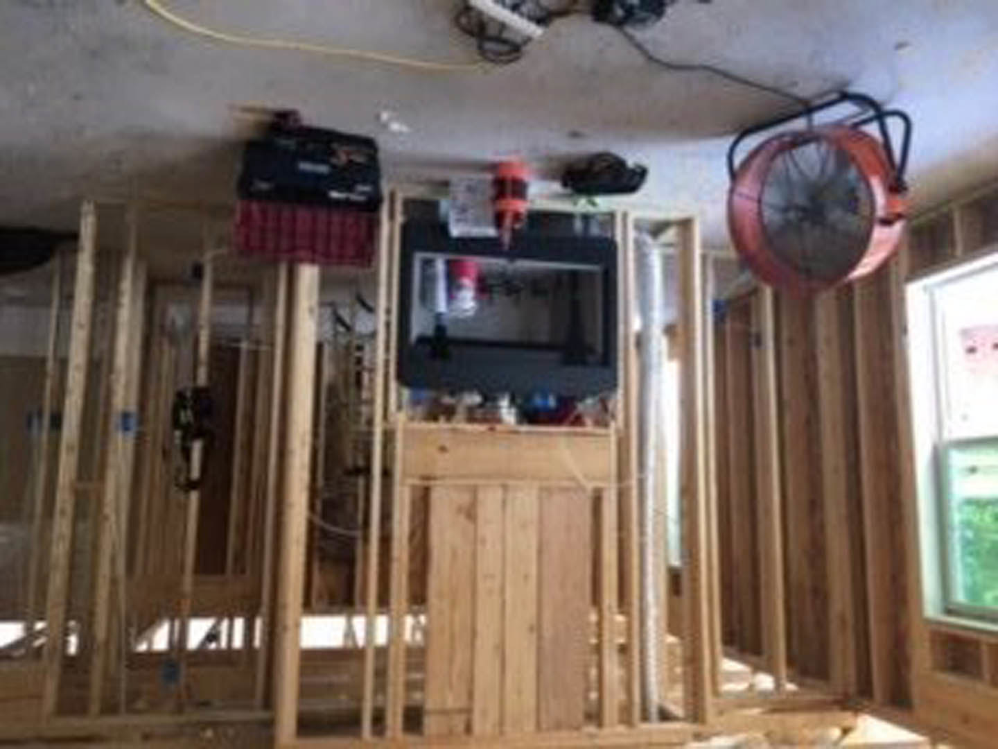 Living room with exposed wood framing, wall-mounted television, ceiling fan, and wood plank accent wall.
