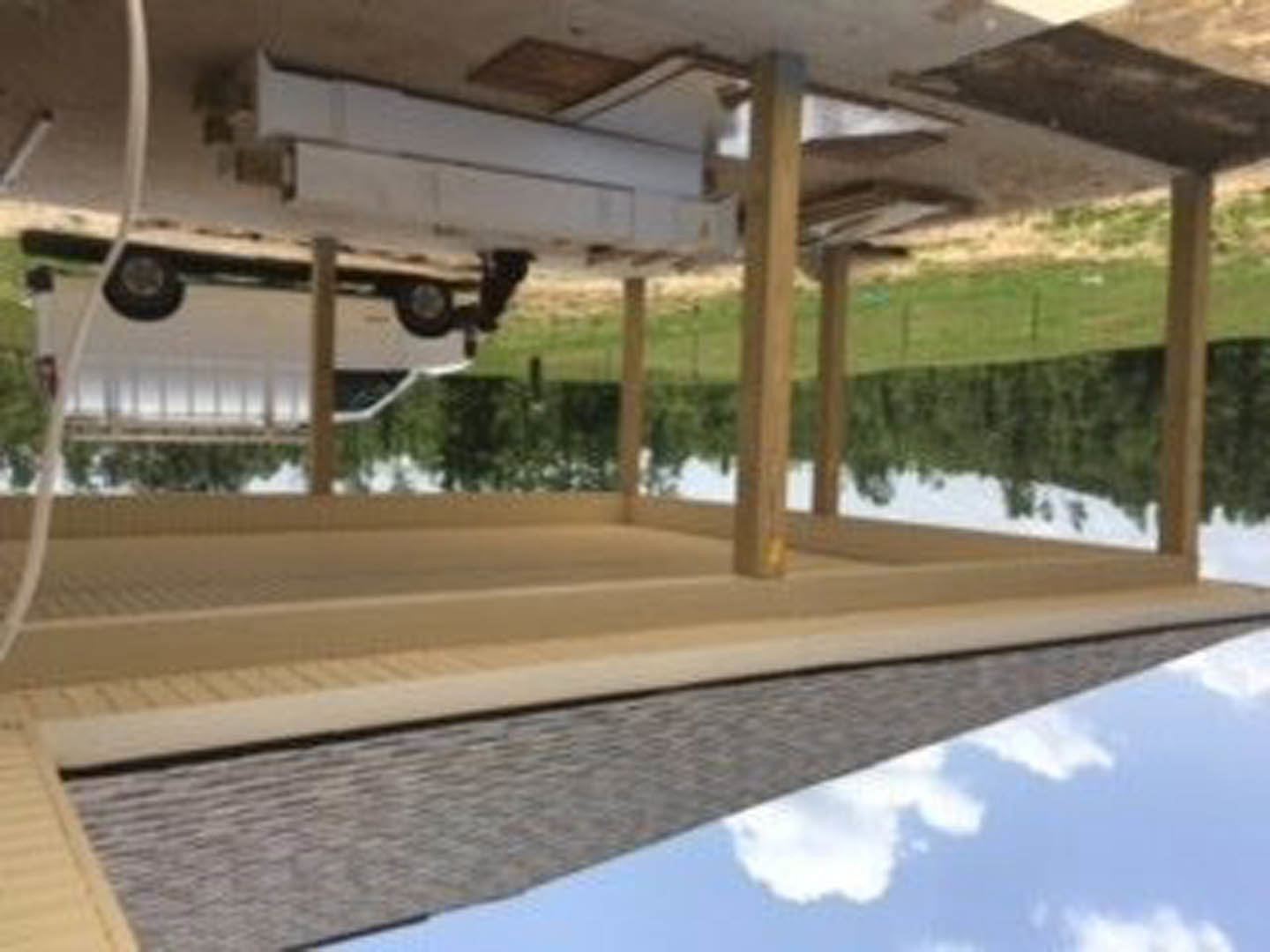 Silver sedan parked beneath a wooden carport with exposed beams, surrounded by trees and cloudy sky, adjacent to a modern home exterior with large windows.