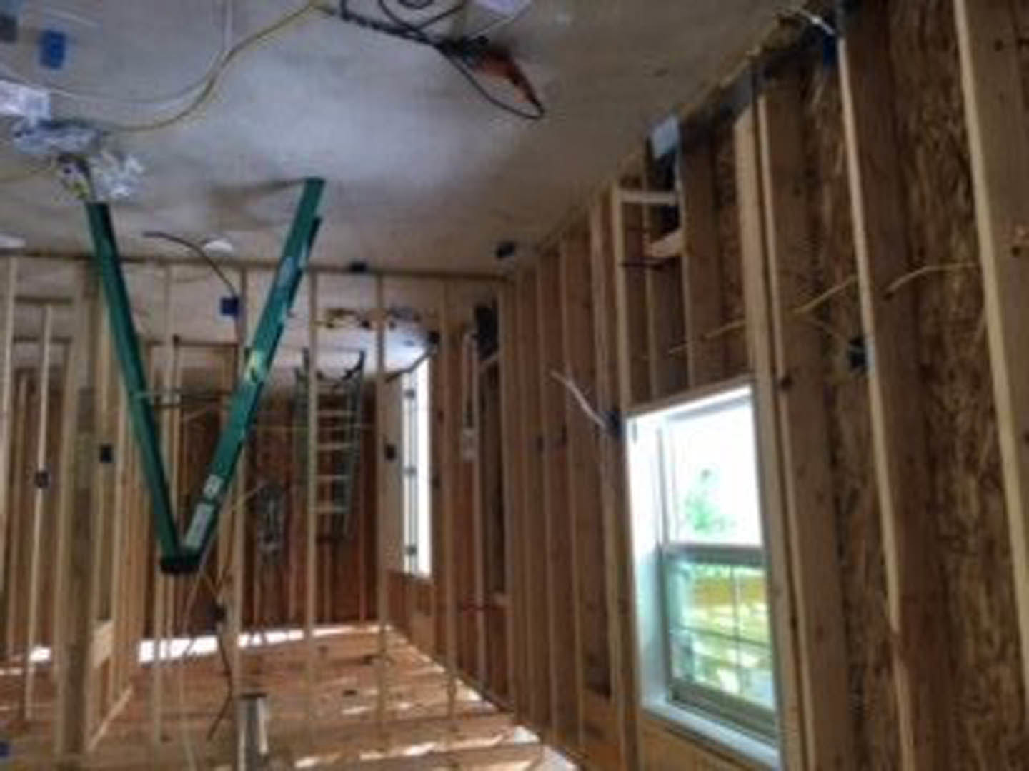 Unfinished room with exposed wood beams, wall insulation, white floor, window overlooking outdoors, and a ladder leaning against the wall