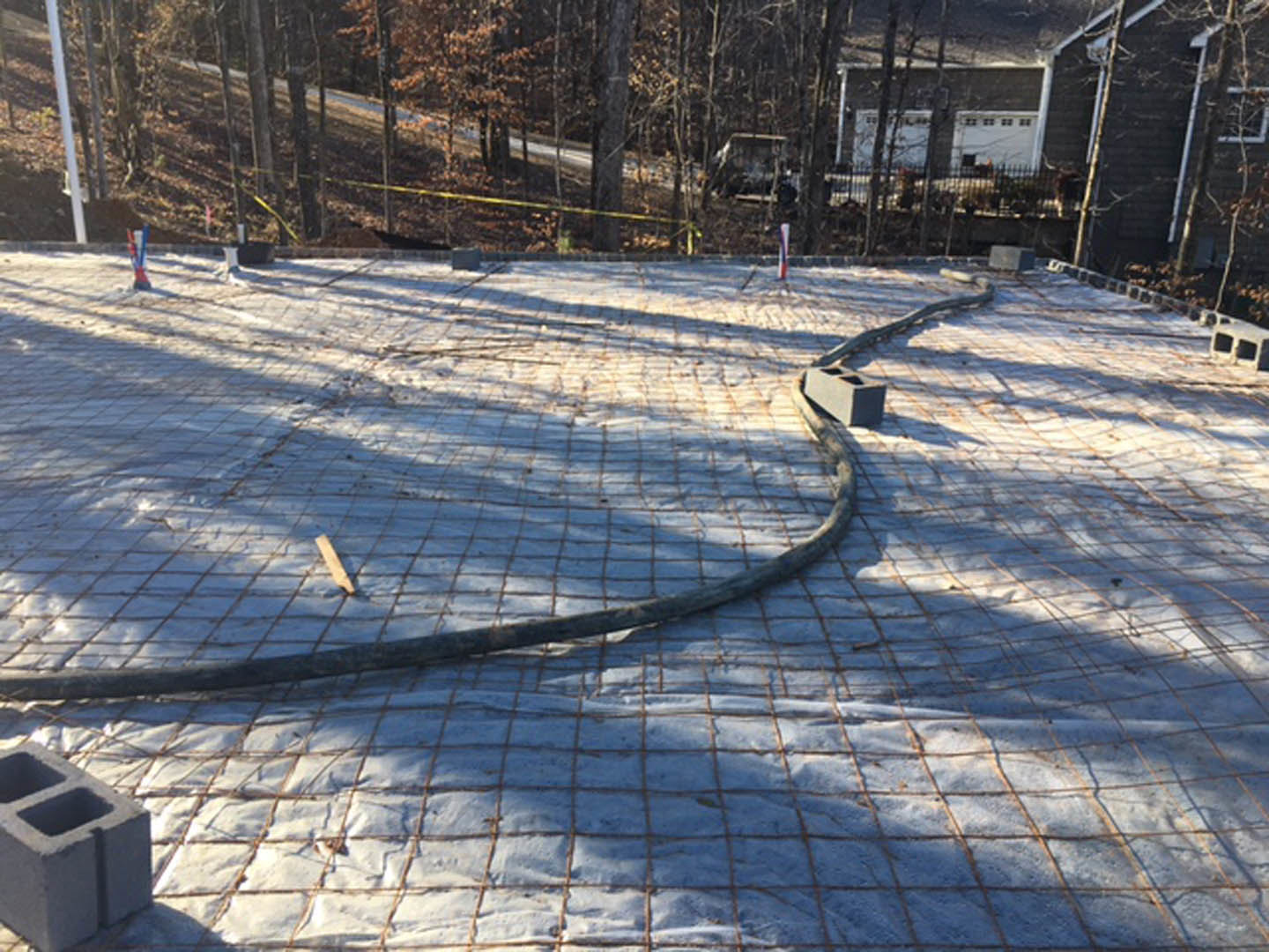 Concrete slab with exposed wire and scattered snow, bordered by a metal fence and gate, winter trees in background.
