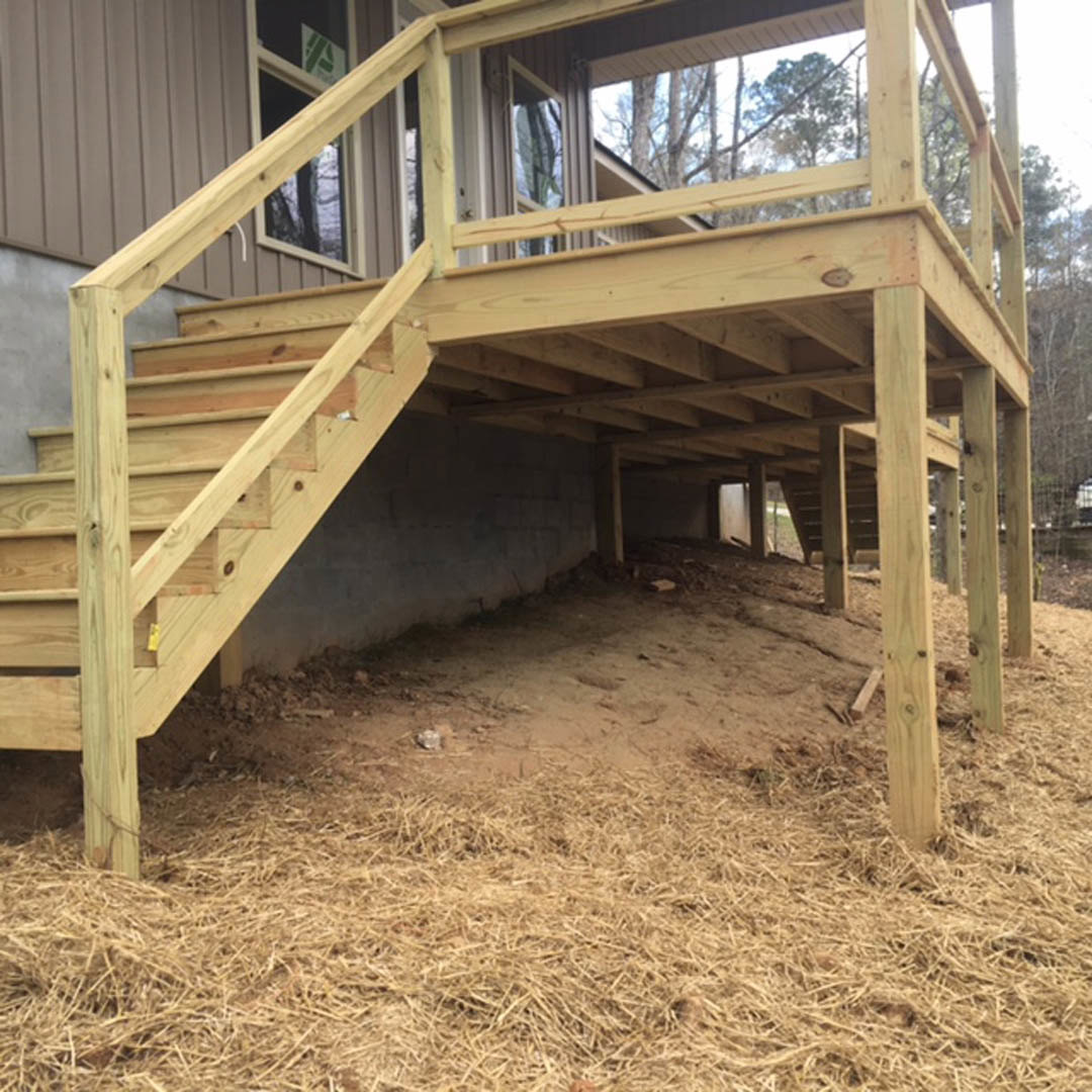 Wooden deck with porch, hay-covered wall, straw scattered on ground, wooden railing, trees in background