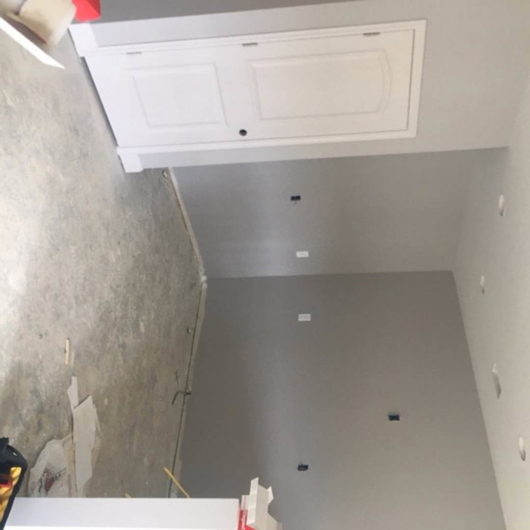Gray painted wall with white trim, white door featuring a central hole, light-colored flooring, and partial view of kitchen cabinetry and countertop