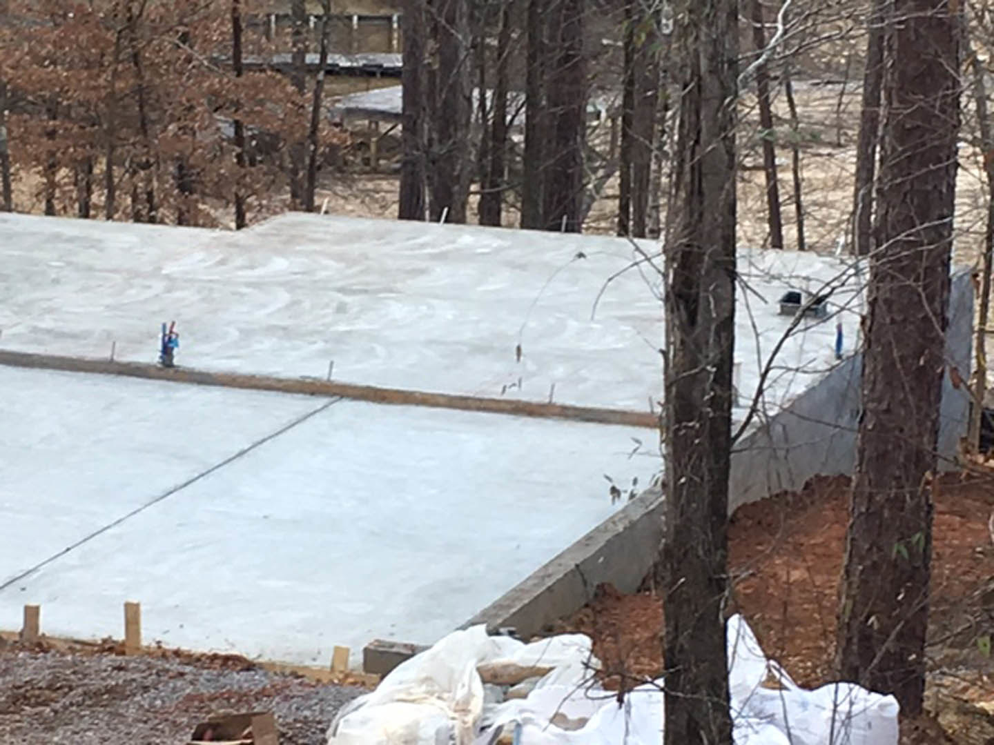 Concrete slab foundation surrounded by snow and trees, person standing on surface, winter landscape in background