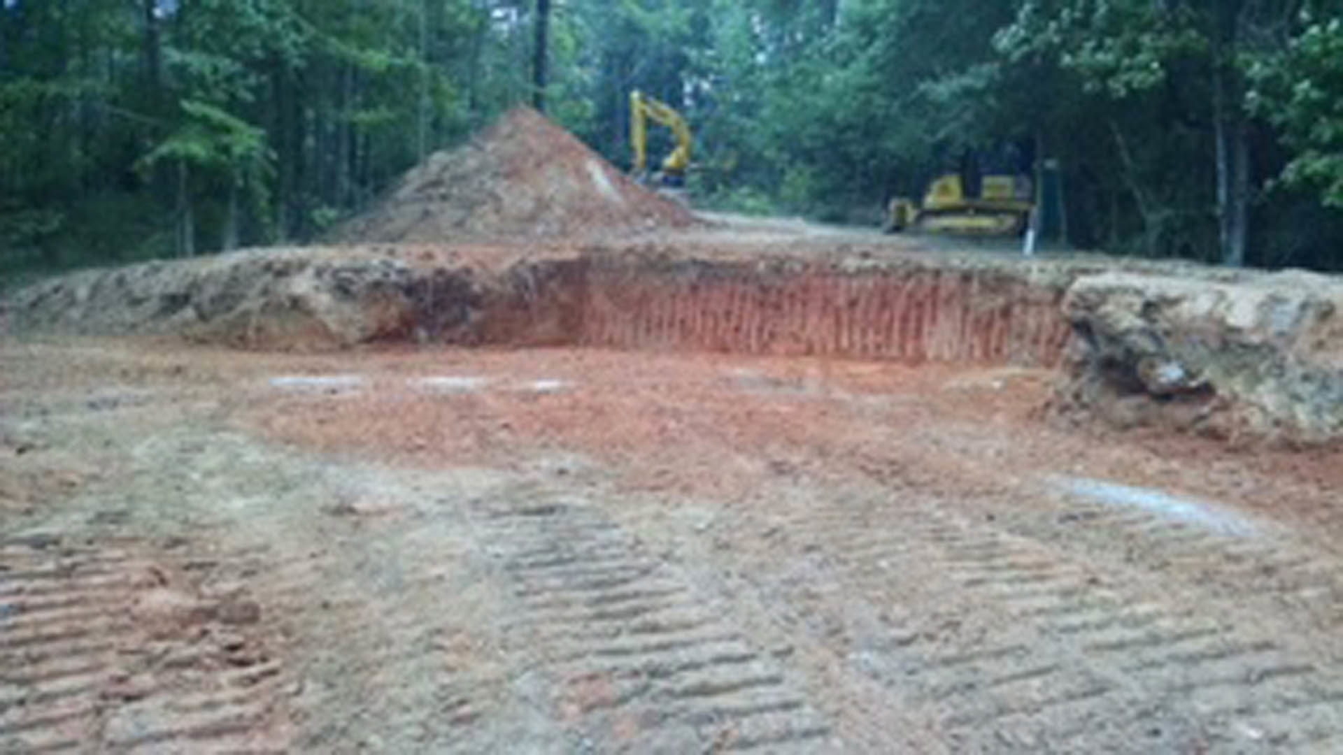 Dirt pit with tire tracks, surrounded by soil and sparse trees, outdoor construction site with uneven ground