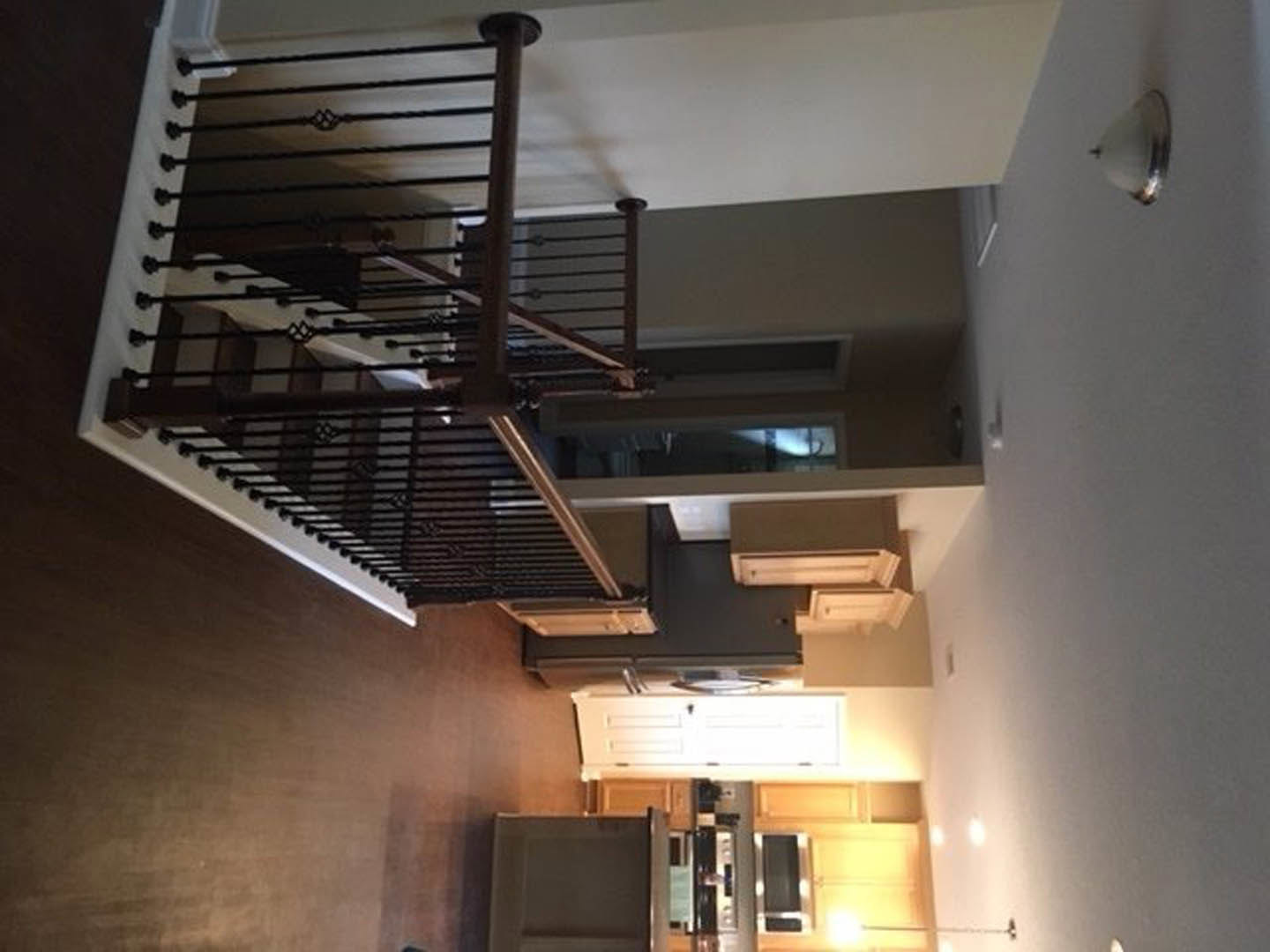 Wood staircase with metal handrail, white plaster walls, recessed ceiling lighting, exposed ceiling beam, and partial view of window.
