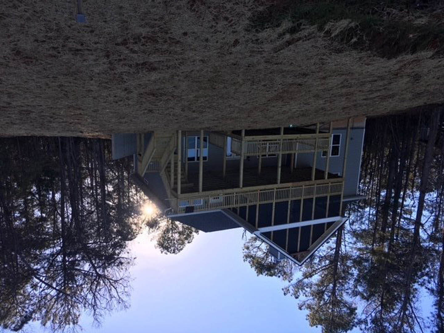 White custom home with covered front porch, large windows, and expansive green lawn; tree branches visible in foreground, winter sunlight highlighting exterior finishes.