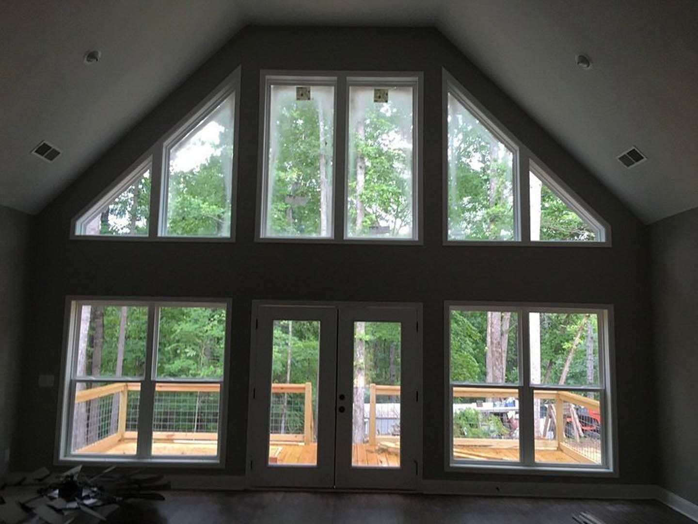Spacious room featuring wide double glass doors opening to a deck, large windows with tree views, light walls, and window blinds.