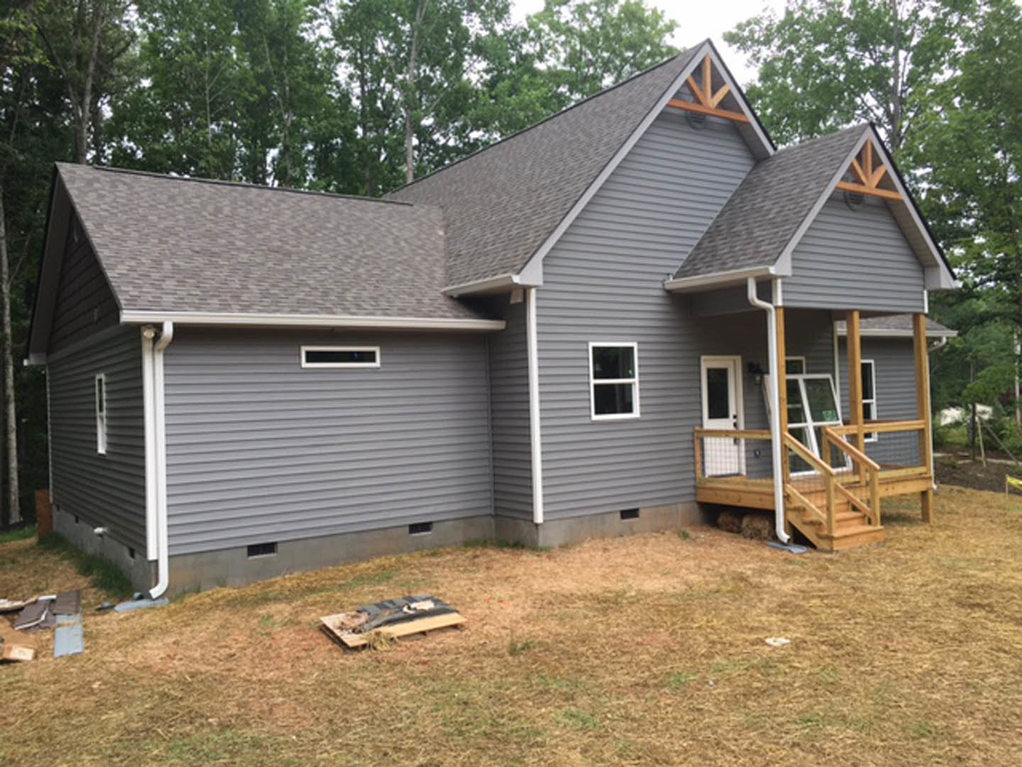 Two-story home with light siding, covered front porch, white-framed windows, white door with black screen, wooden deck, and surrounding trees.