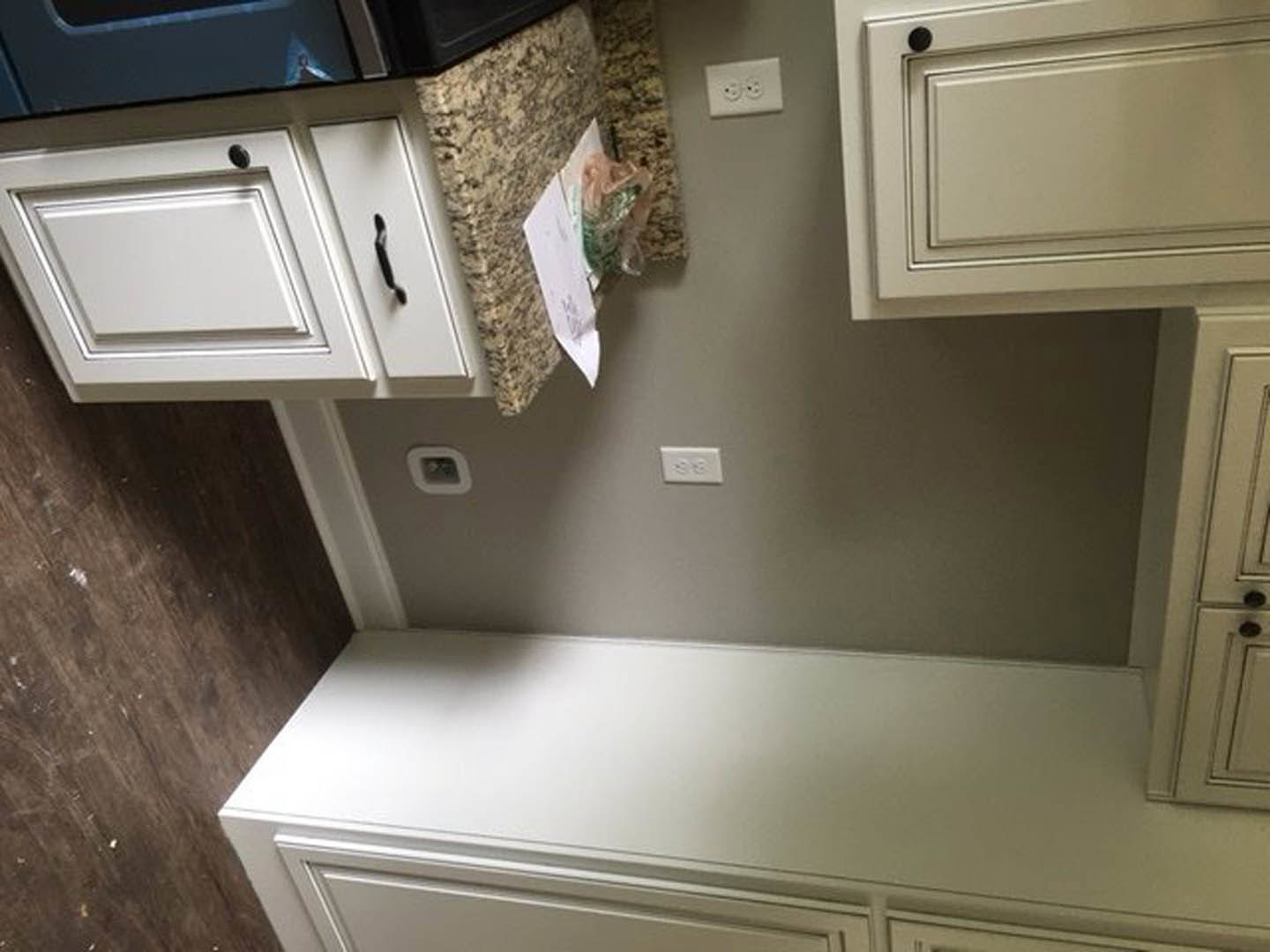 White kitchen cabinets with black hardware, marble countertop, stainless steel sink, and white electrical outlets on the backsplash