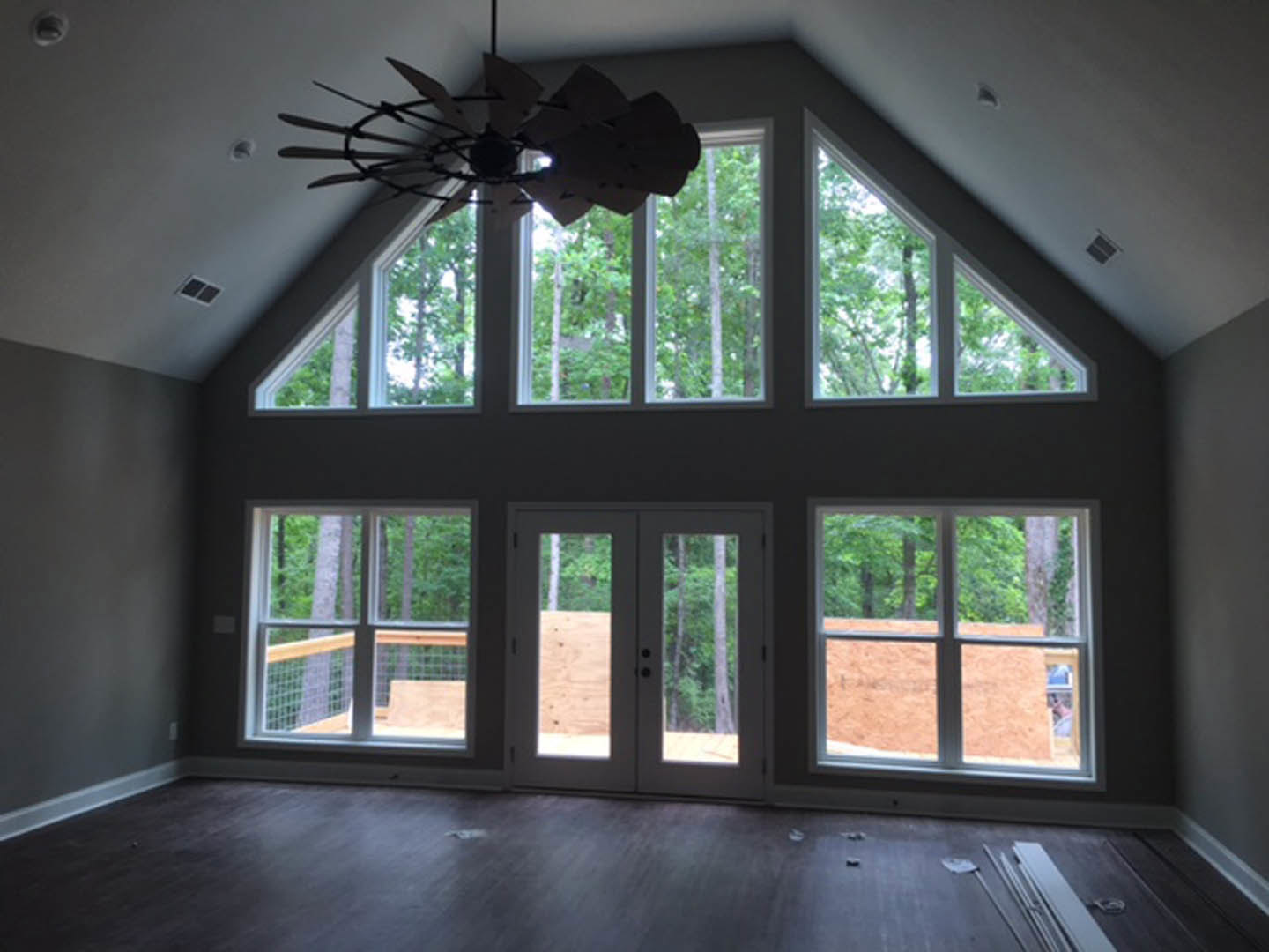 Spacious room with large windows, ceiling fan, double glass-panel doors, light-colored walls, and hardwood flooring