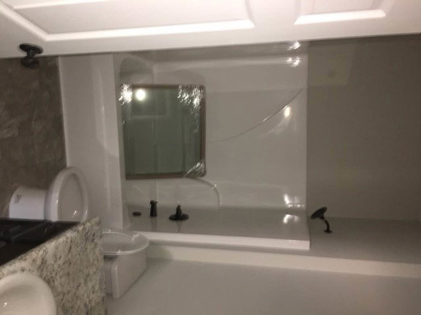 Modern bathroom featuring a rectangular mirror above a white sink with chrome faucet, black and white countertop, tiled walls, and bathtub partially visible.