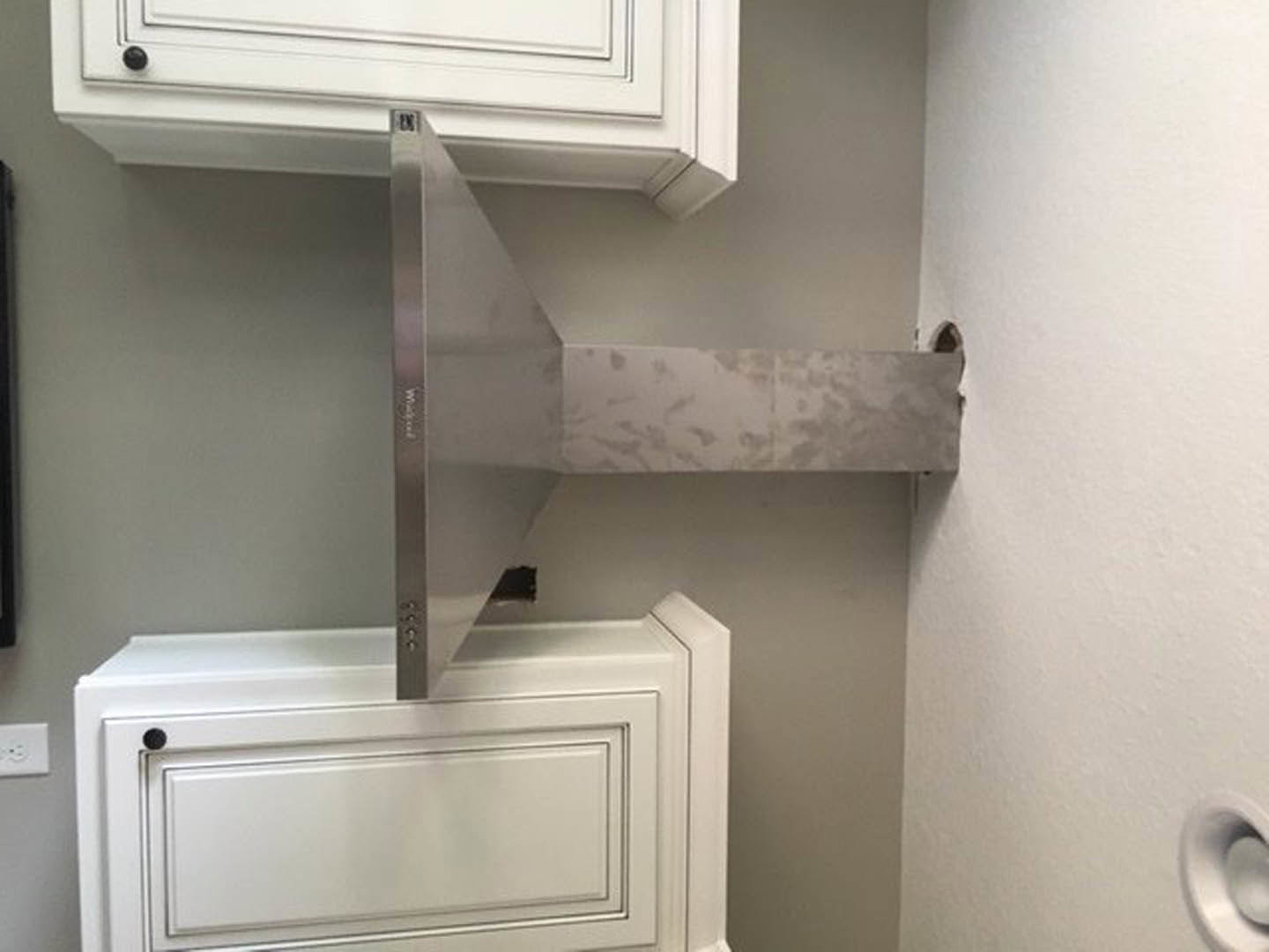 Stainless steel vent hood above white kitchen cabinets with metal handles, plaster walls, and built-in drawers