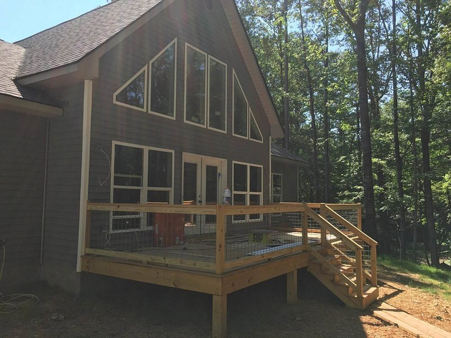 Two-story home with wood siding, spacious deck, covered porch, white-framed windows, wooden fence, and mature trees in the background