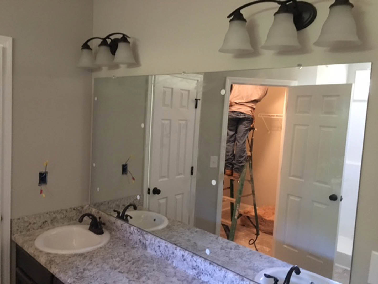 Bathroom with white tile walls, modern sink and faucet, round bowl, light fixture, man on ladder near mirror