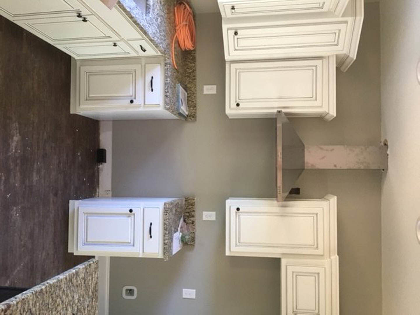 White kitchen with shaker cabinets, black handles, marble countertops, stone backsplash, and white light switch on plaster wall