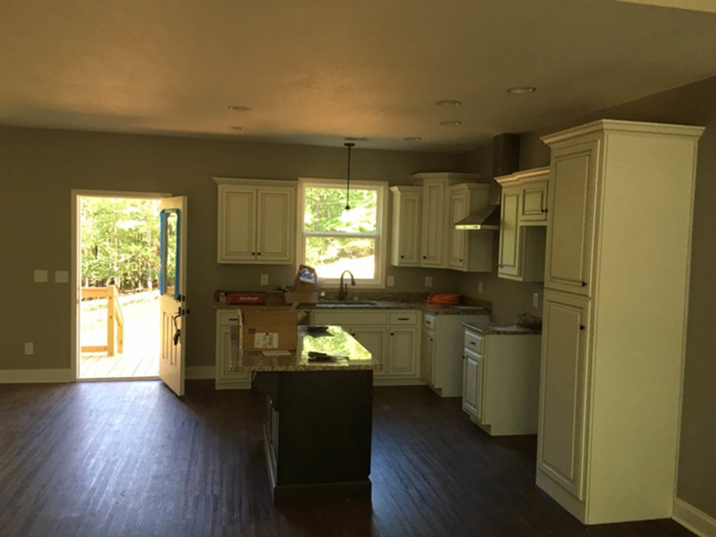 Kitchen with light wood flooring, white cabinetry, black countertop, stainless steel faucet, and a window allowing natural light.