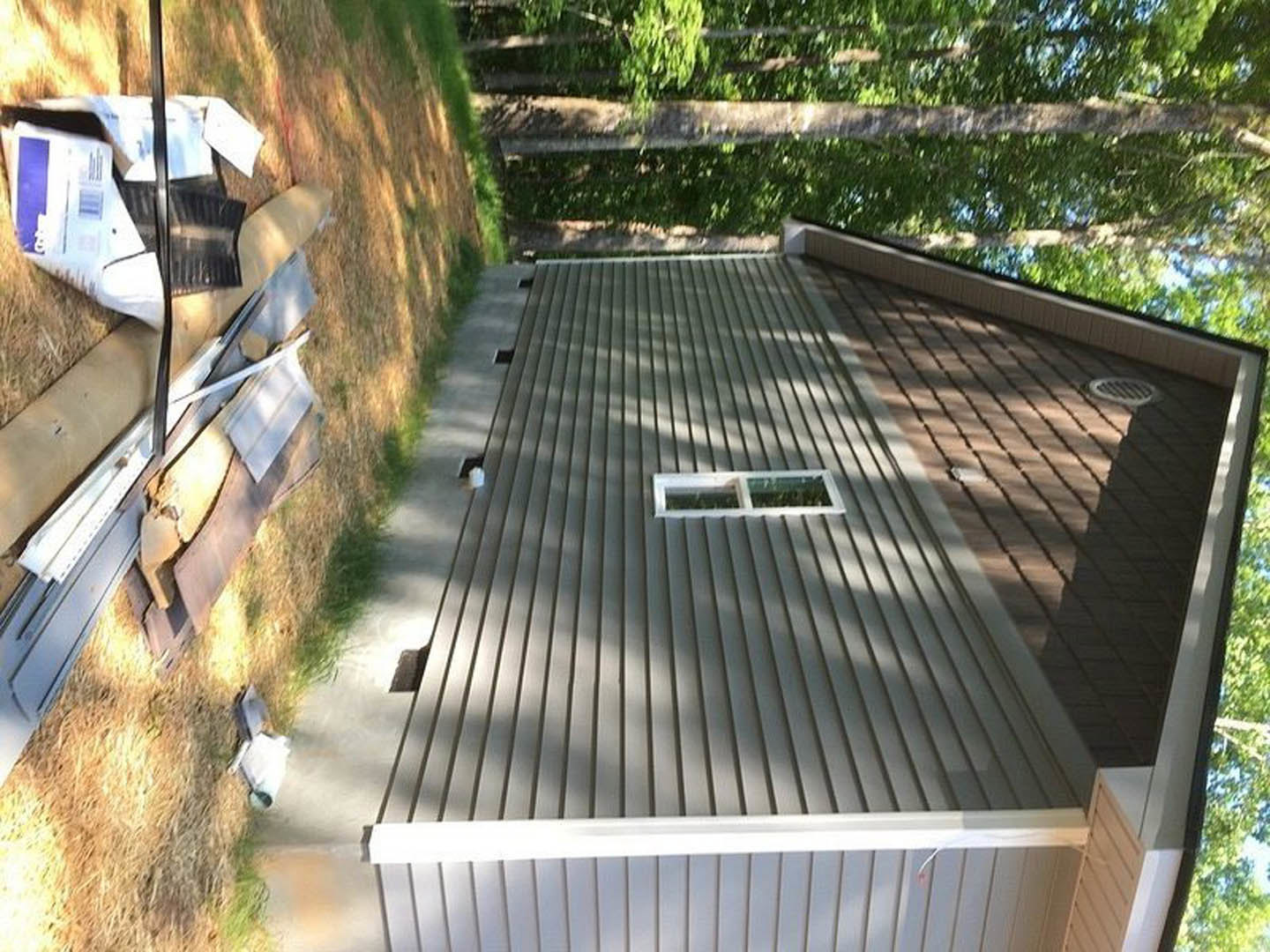 Two-story house with attached garage, white-framed windows, vent, green lawn, trees in background, metal drain cover near driveway