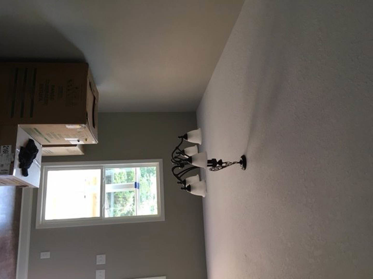 Brushed metal wall sconce mounted on smooth white plaster wall beside window with white trim, illuminated and casting soft light in modern room.