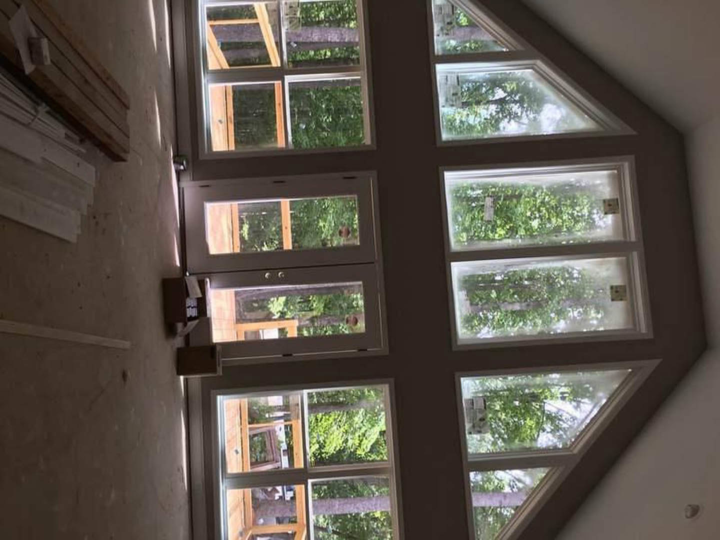 Spacious room featuring multiple large windows, glass double doors, white trim, and a potted green plant with views of leafy trees outside