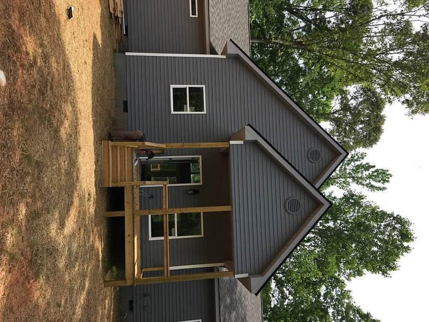 White house with front porch, wooden staircase, white-framed window, exterior wall vent, mature tree in landscaped yard