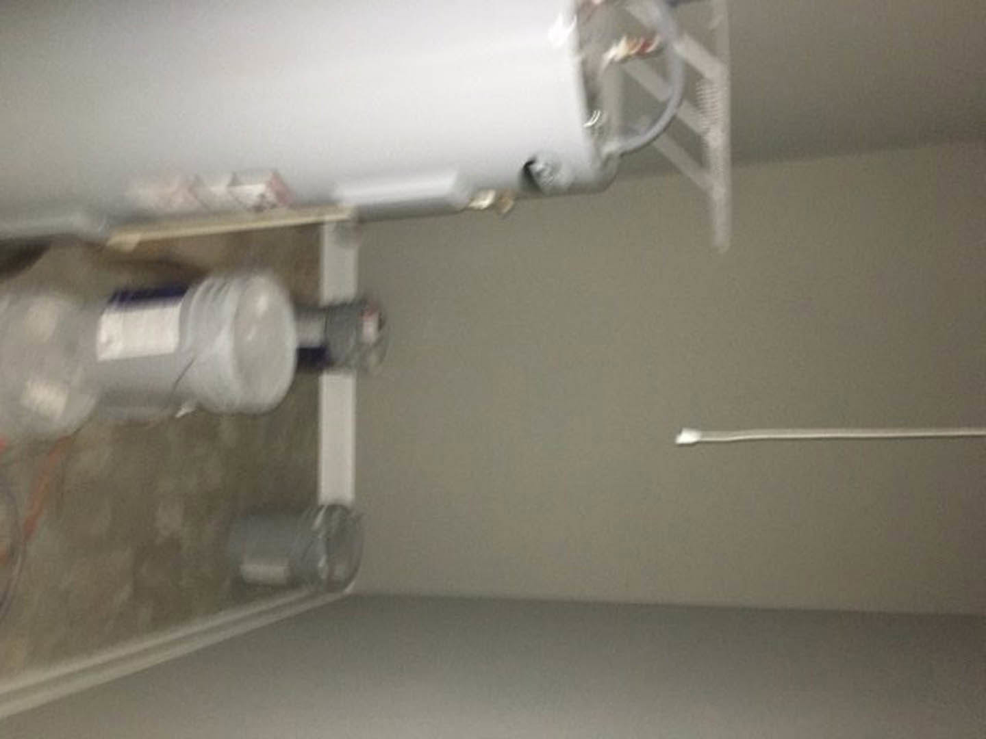 White plaster ceiling with a cylindrical white tank mounted on the wall and a small white object attached to its side