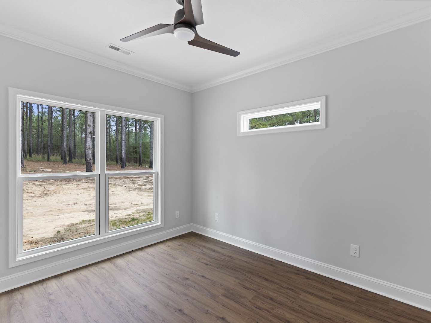 Ceiling fan with white light fixture, large windows showing trees and dirt field, wood laminate flooring, white plaster walls