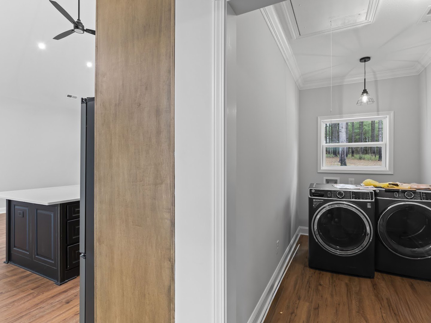Laundry room with white washing machine, light wood cabinetry, laminate flooring, and large window overlooking trees