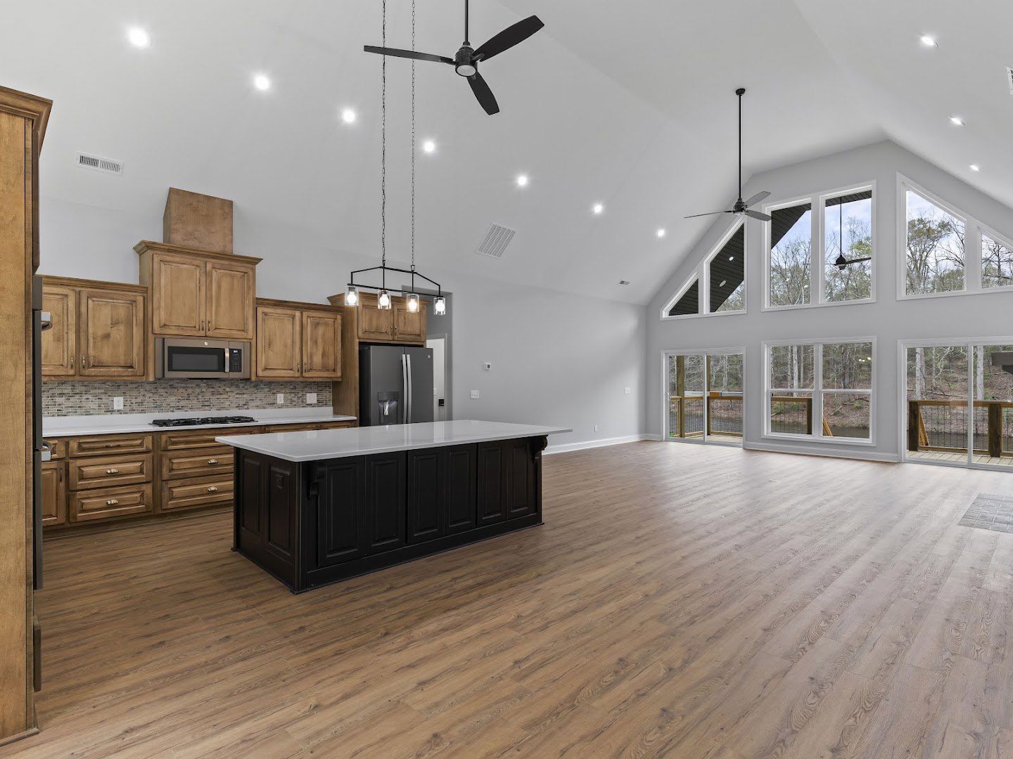 Spacious kitchen featuring black cabinetry with white countertops, wood flooring, stainless steel refrigerator, built-in microwave, and a large ceiling fan with integrated light.