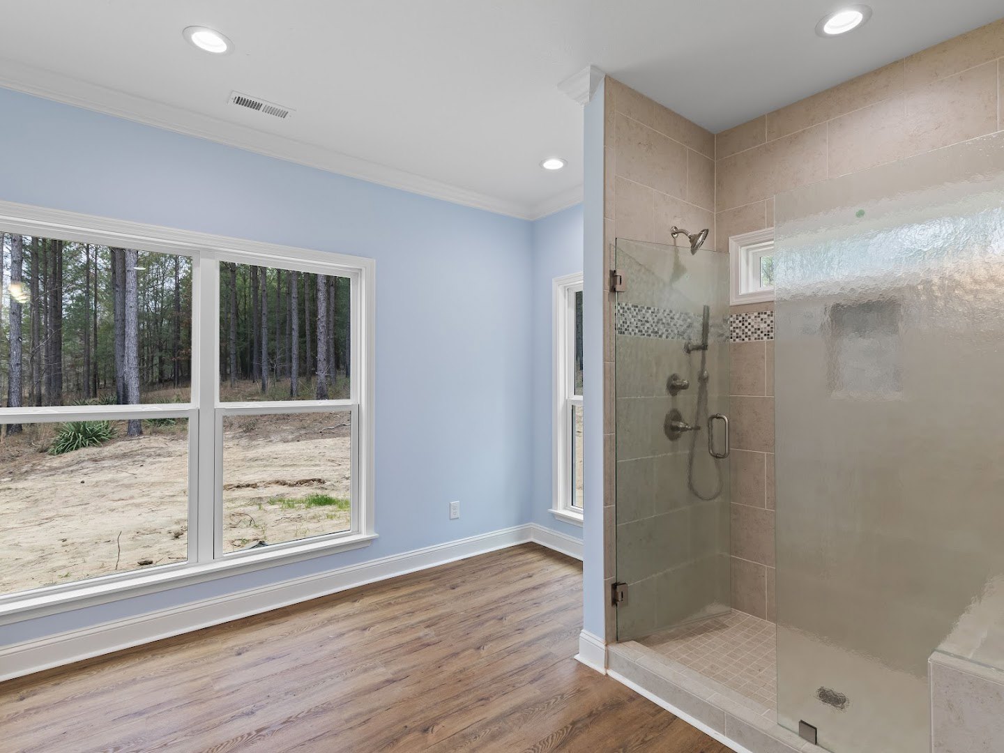 Bathroom featuring a glass-enclosed shower, hardwood flooring, plaster walls, large window with views of trees, and a potted plant near the shower.
