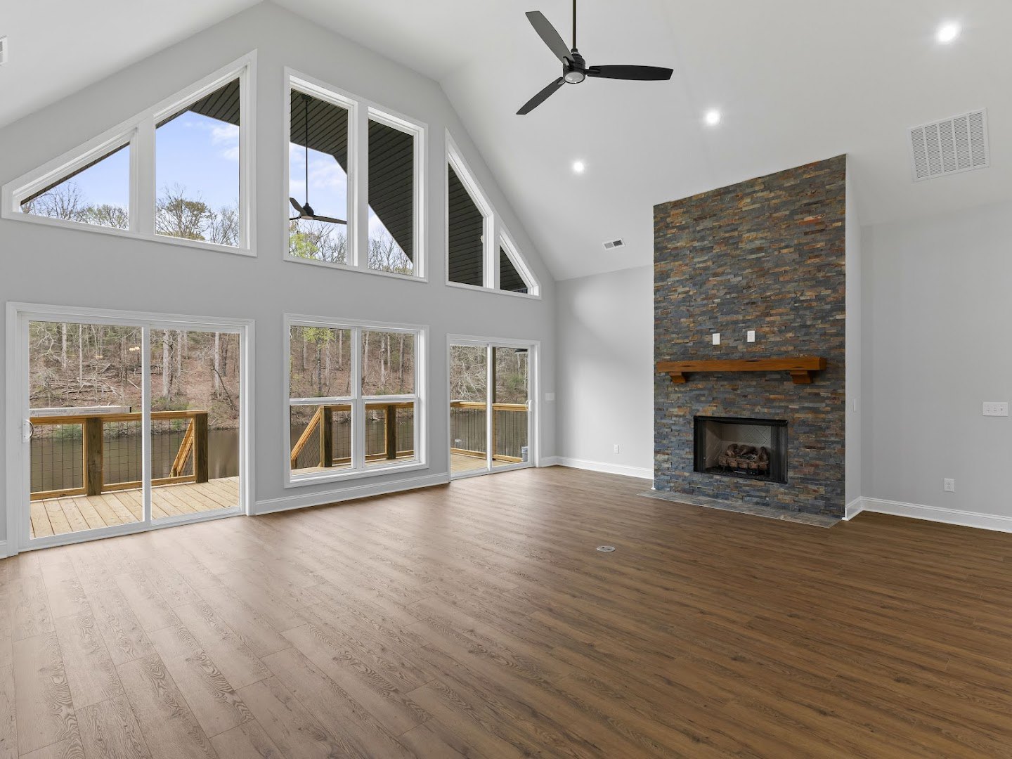 Spacious living area with hardwood floors, ceiling fan with light, fireplace featuring a wood mantel and baskets inside, wall vent, and neutral painted walls
