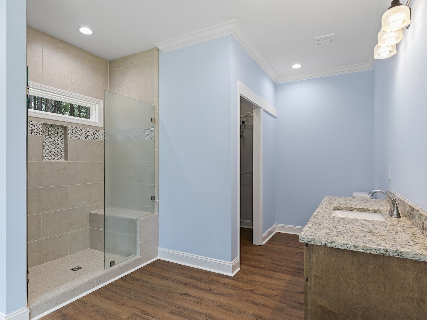 Modern bathroom featuring a glass shower enclosure with gray tile walls, white sink with chrome faucet, and light-colored floor tiles.