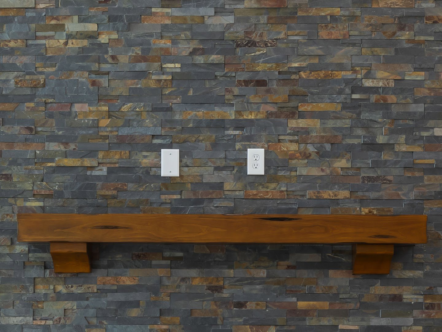 Wooden shelf mounted on red brick wall above stone bench, white electrical outlet visible, person standing beside wooden table