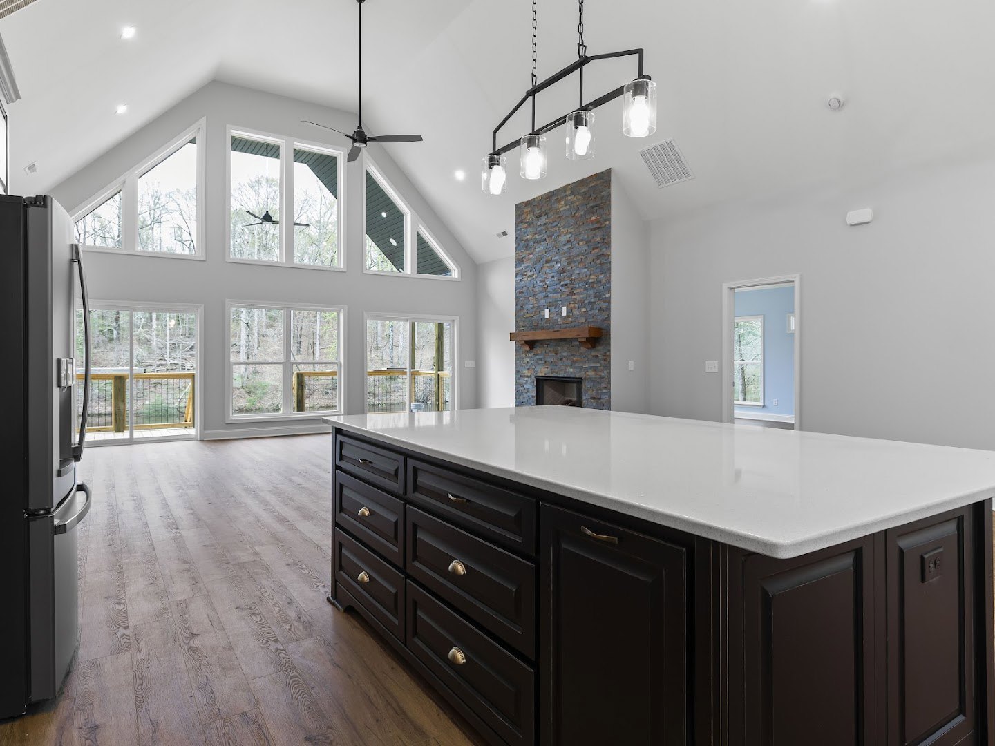 Spacious kitchen featuring a large white countertop island with black cabinets, stainless steel refrigerator, windowed door, and modern wall light fixture.